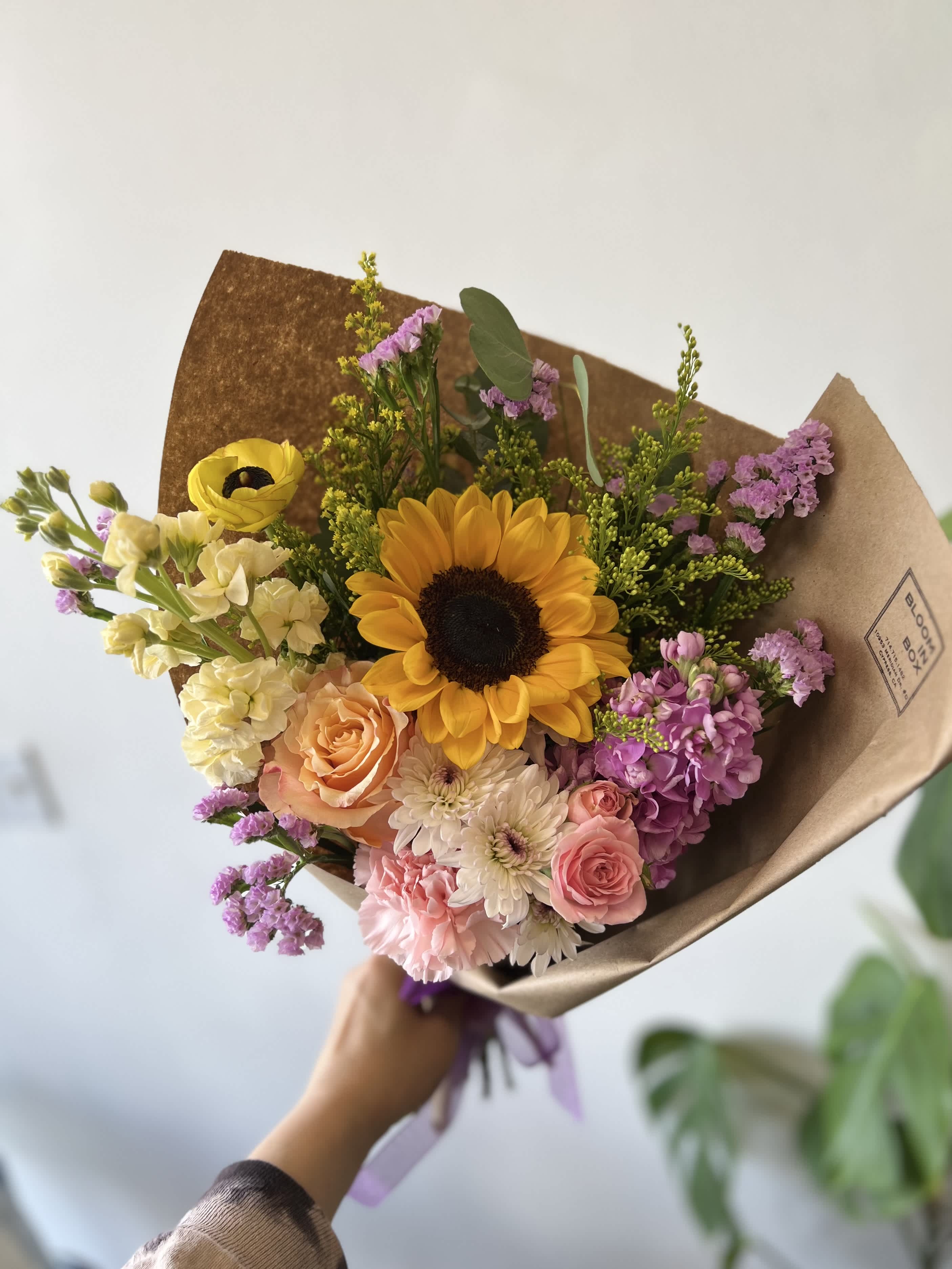 Hand-tied bouquet with a sunflower, roses, and pastel blooms in brown paper