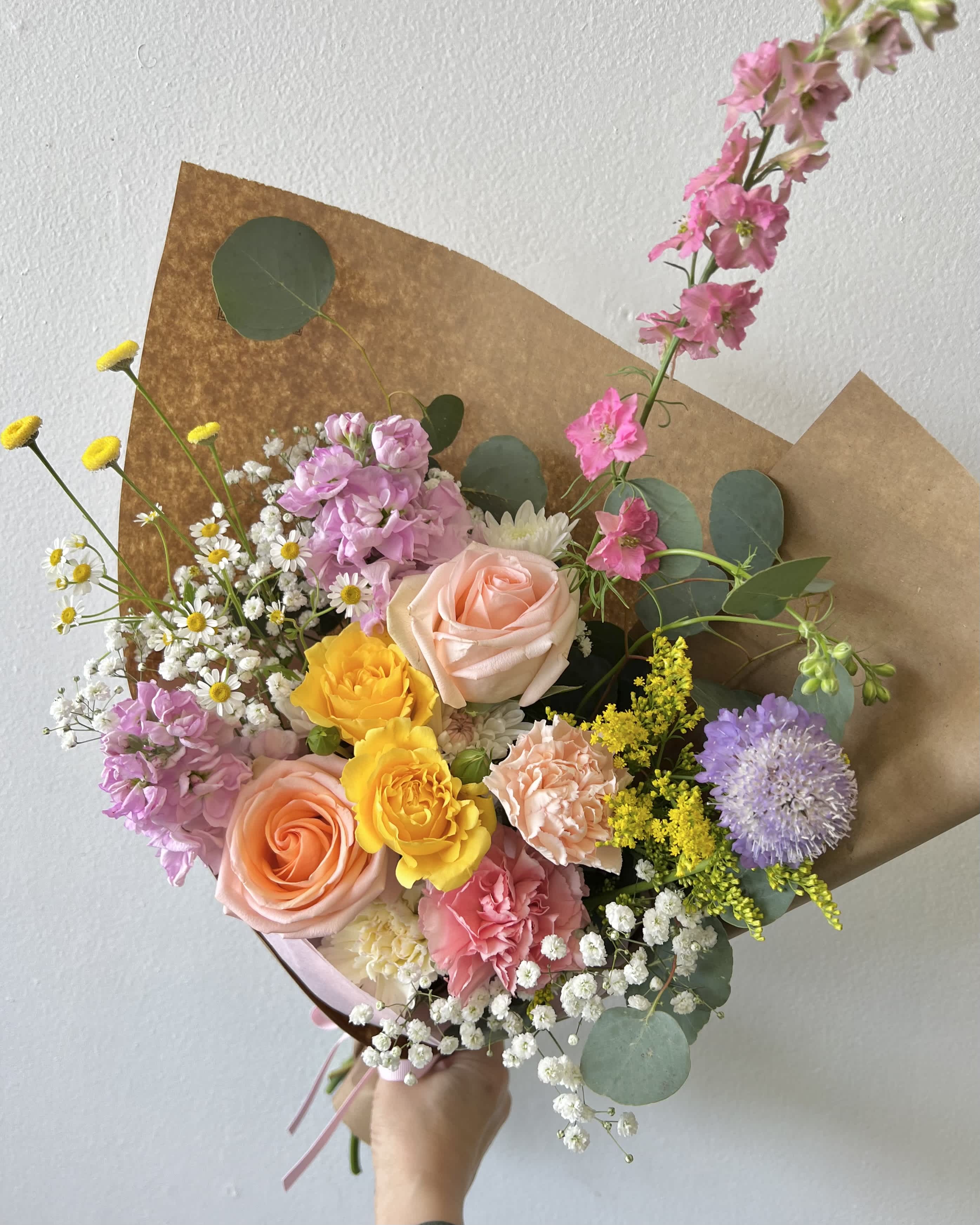 Hand-tied bouquet of pink, peach, and yellow flowers wrapped in brown paper
