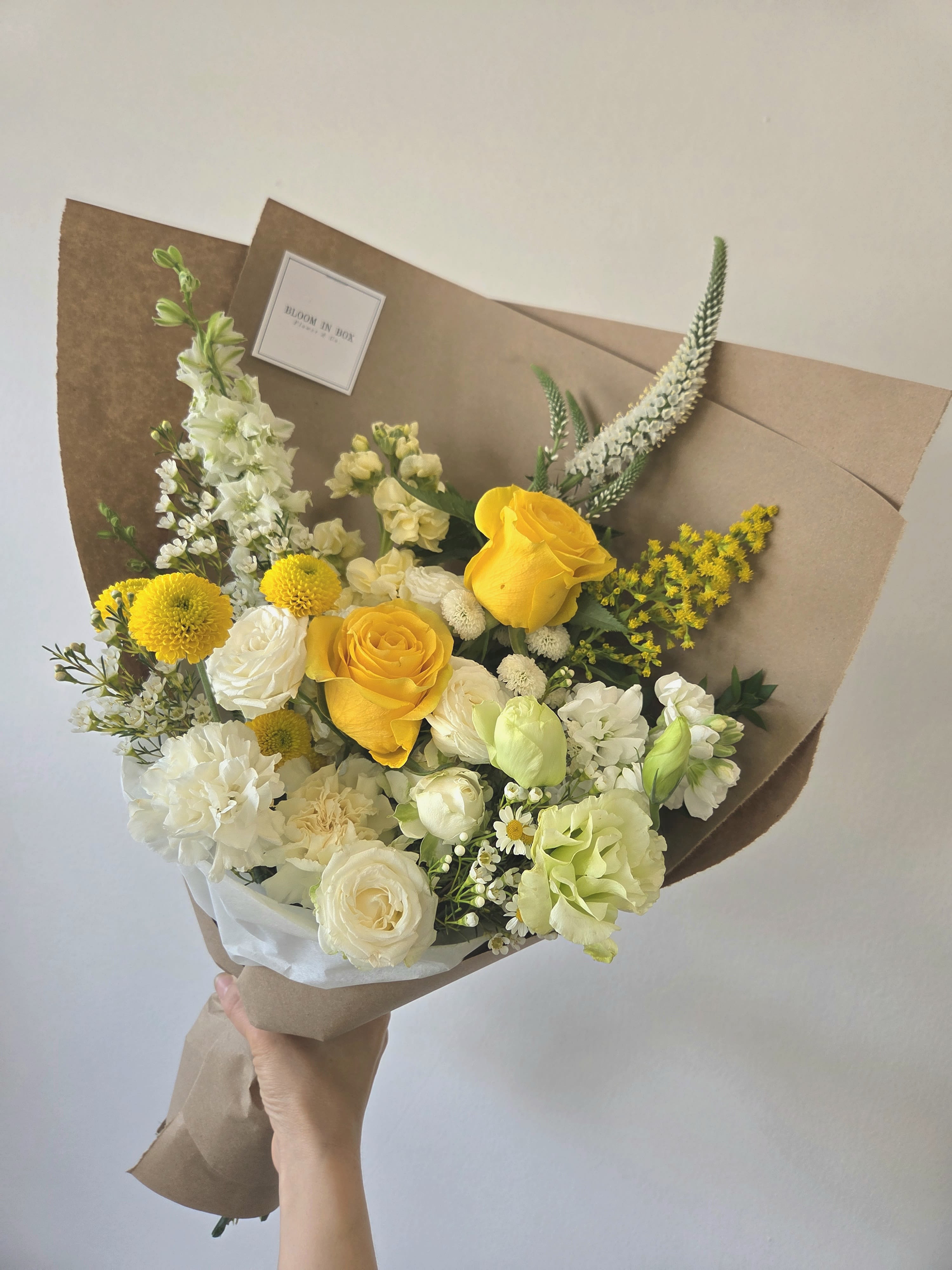 Hand-tied bouquet of yellow and white flowers wrapped in brown paper
