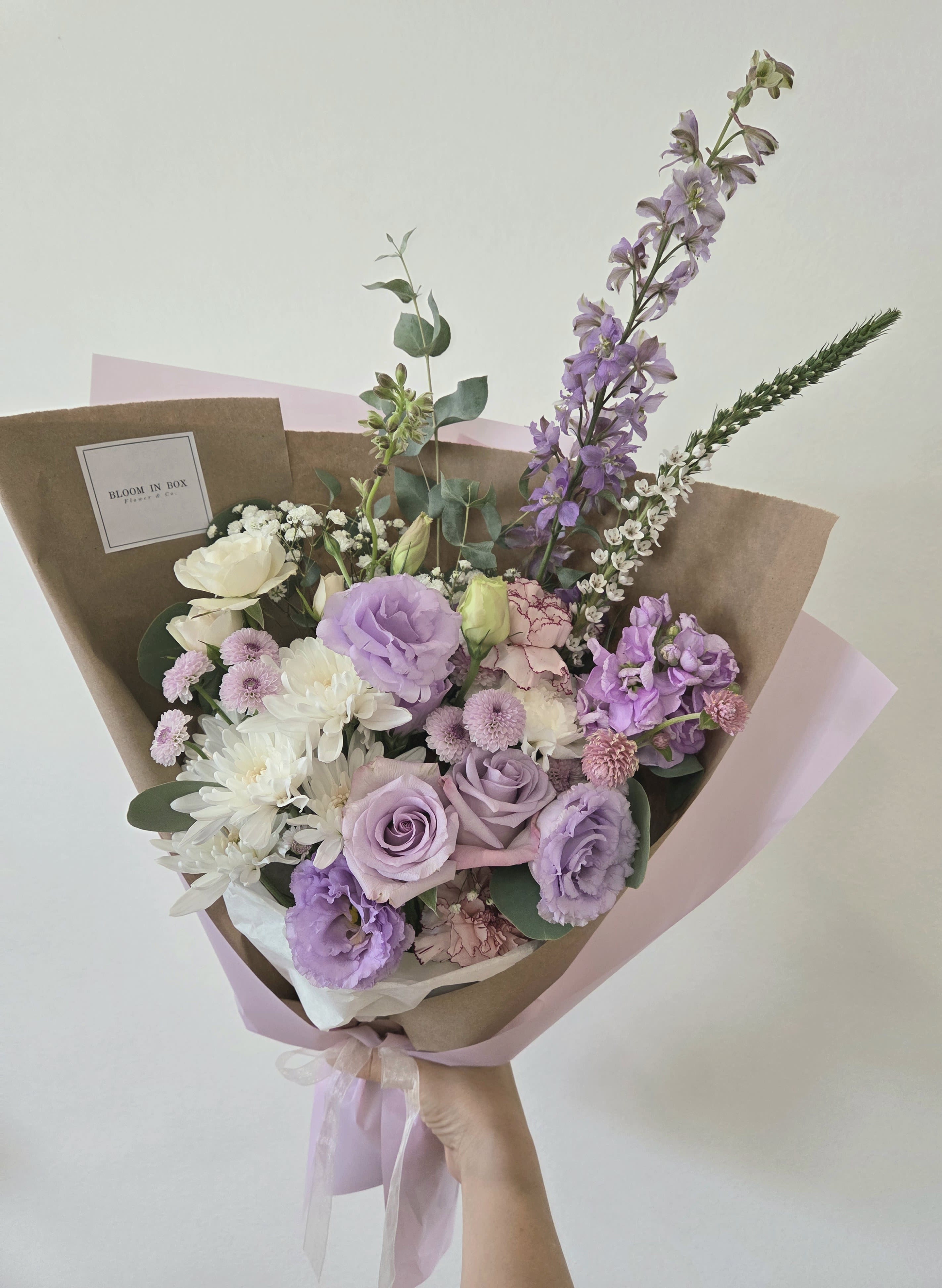 Hand-tied bouquet of lavender, white, and pink flowers wrapped in brown paper