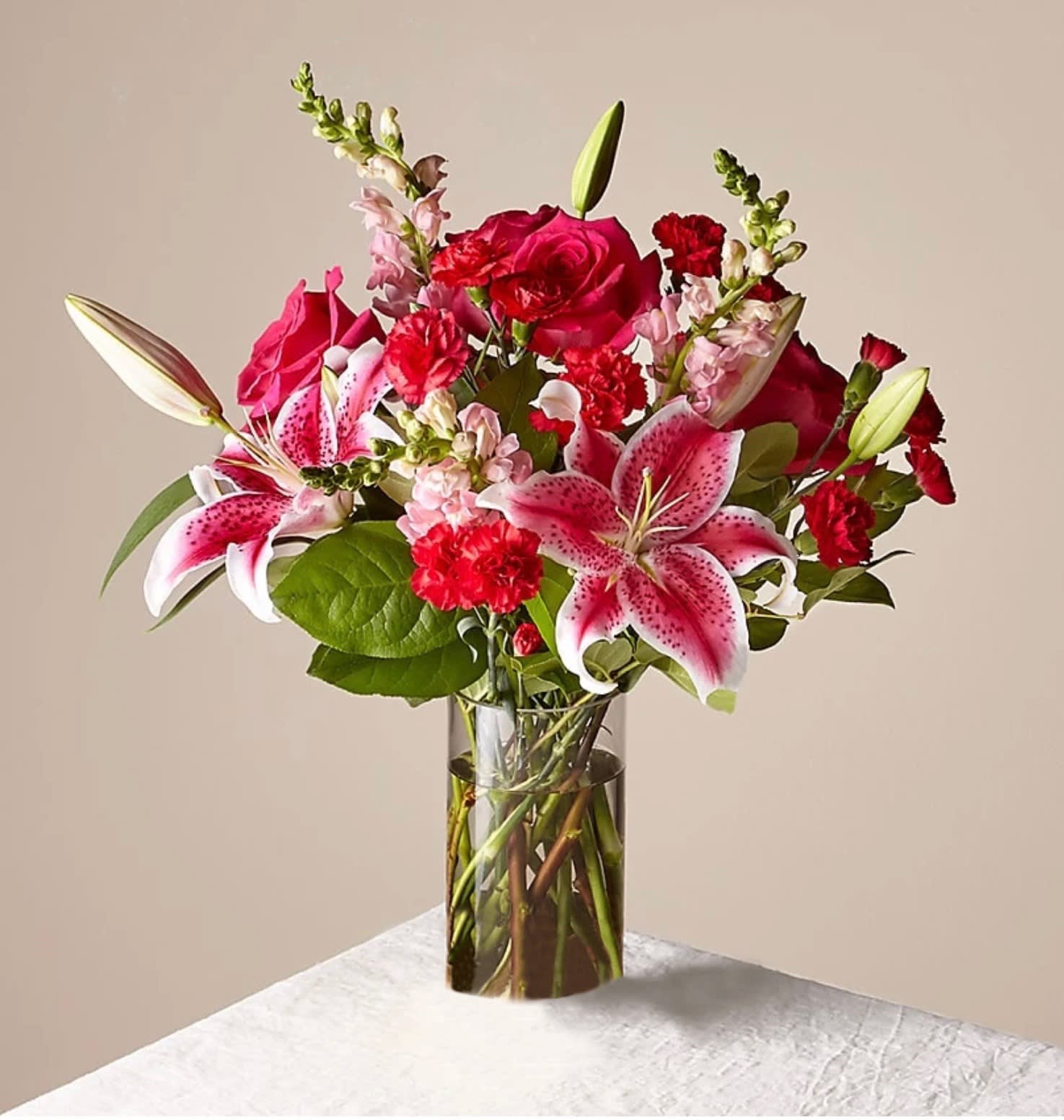 Bouquet of pink lilies, red roses, and carnations in a clear glass vase