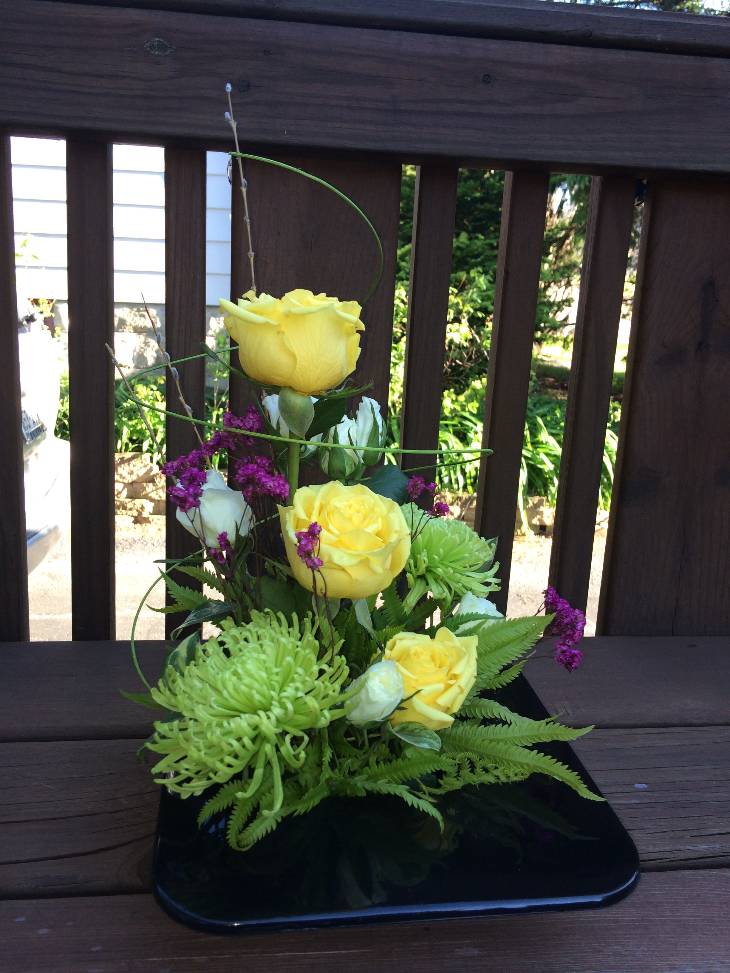 Yellow roses and green chrysanthemums in a black vase with purple accents