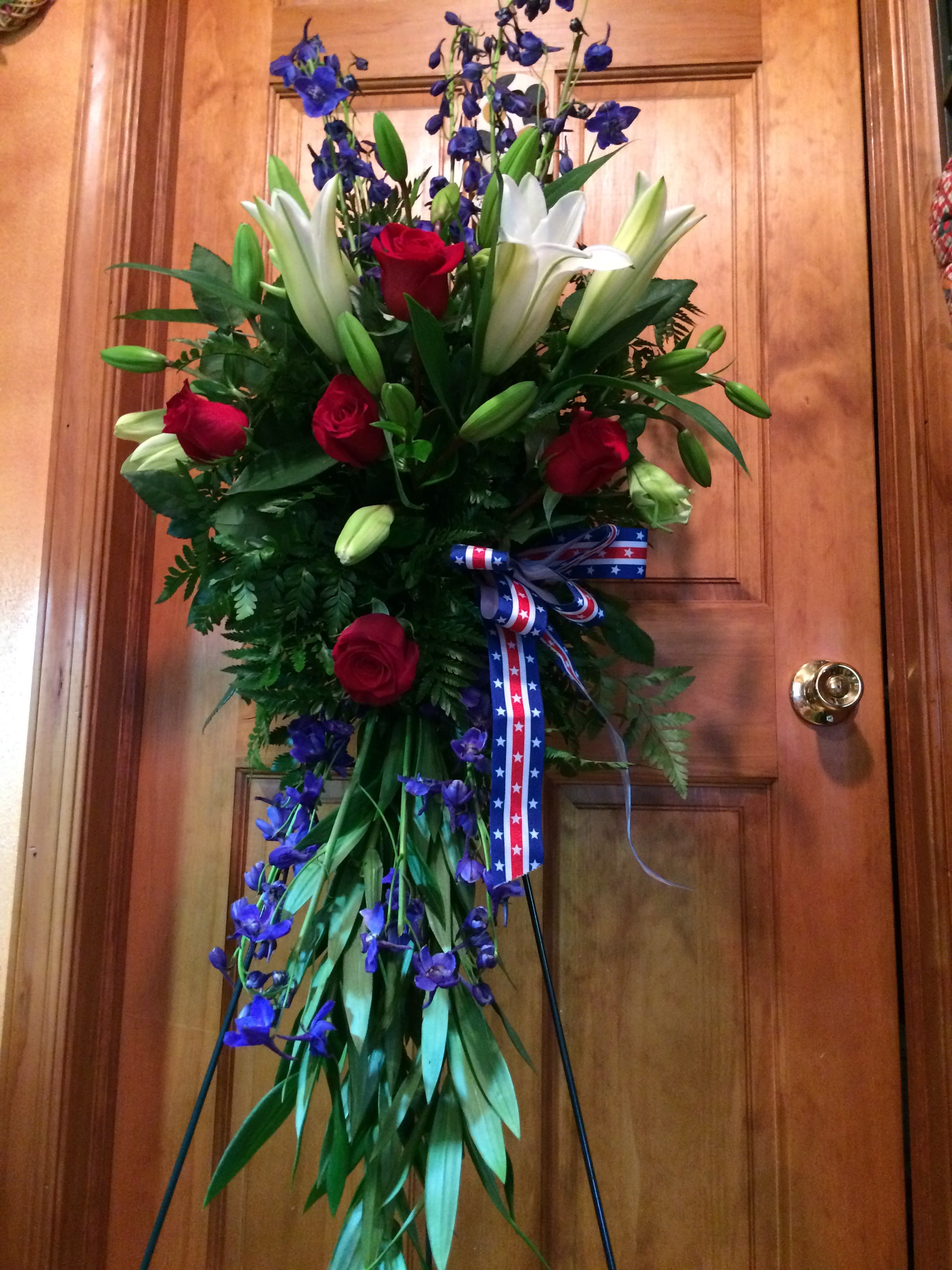 Tall floral standing spray with red roses, white lilies, and blue flowers