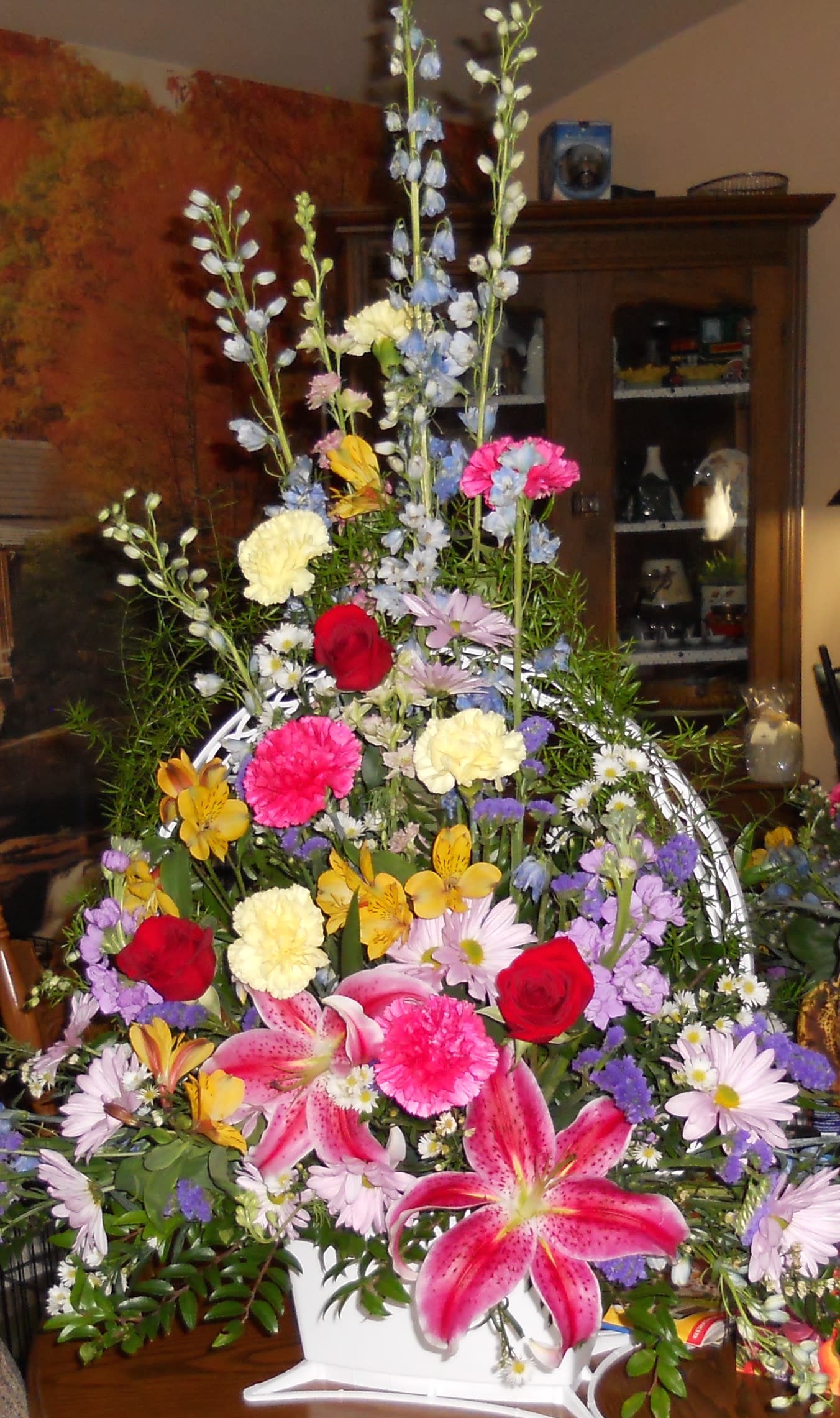Tall mixed flower arrangement in a white container with pink lilies and red roses