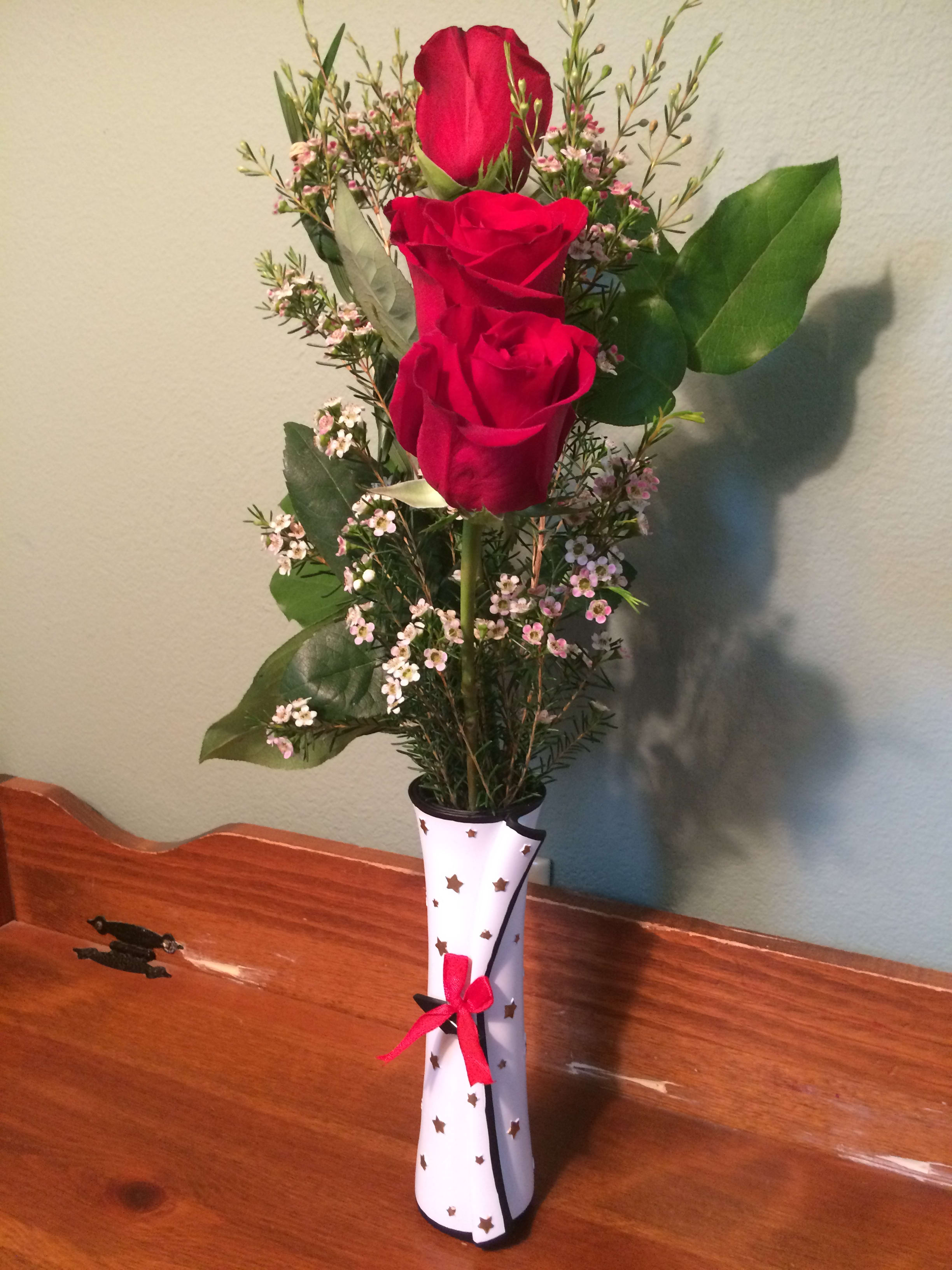 Three red roses in a decorated vase with small pink filler flowers