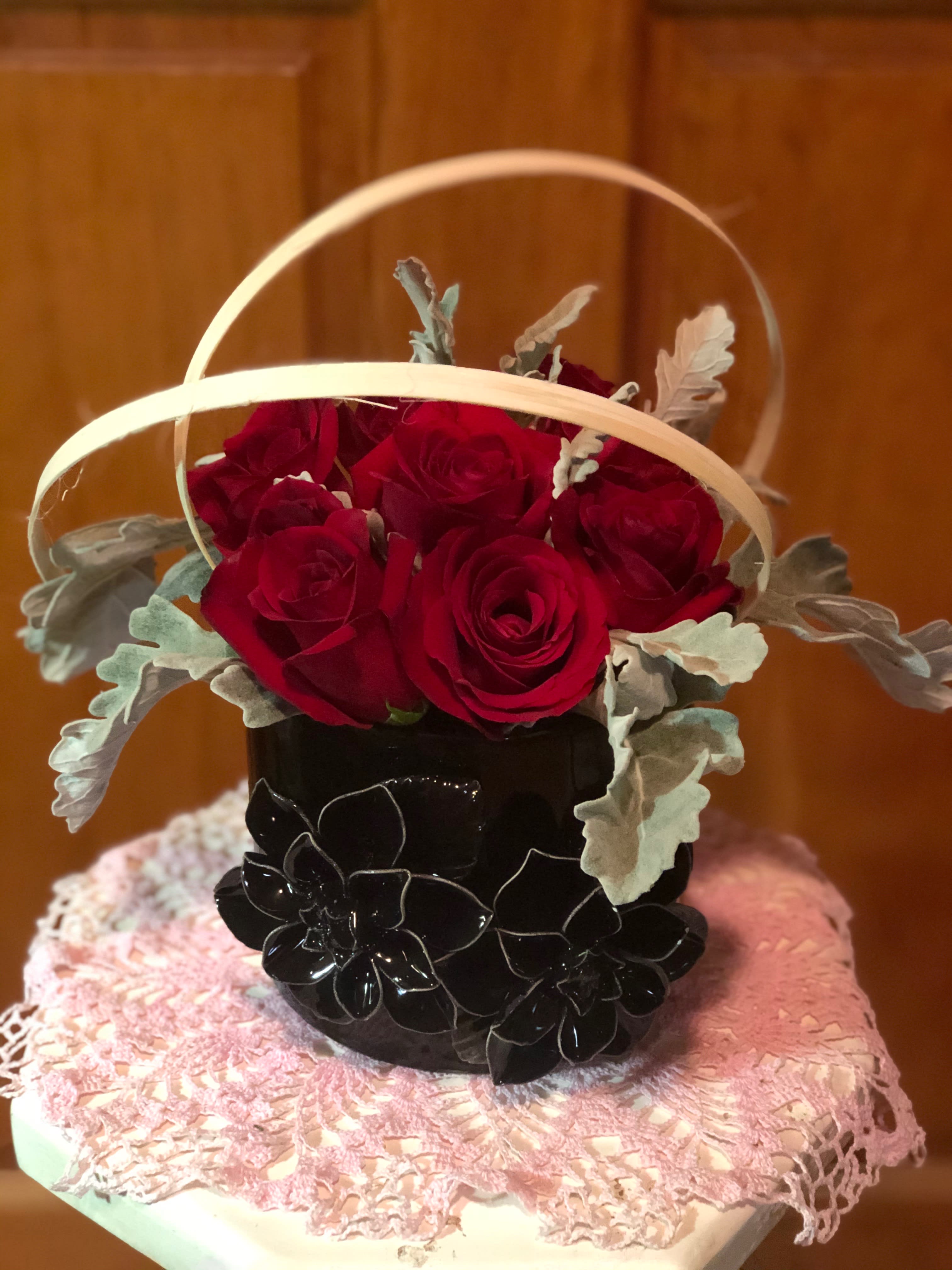 Basket arrangement of red roses with pale foliage in a black container
