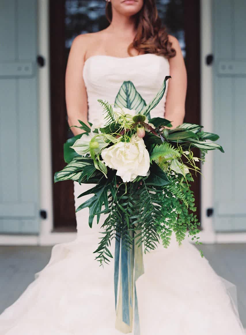 Bride holding a white bouquet with lush green foliage and long ribbon streamers