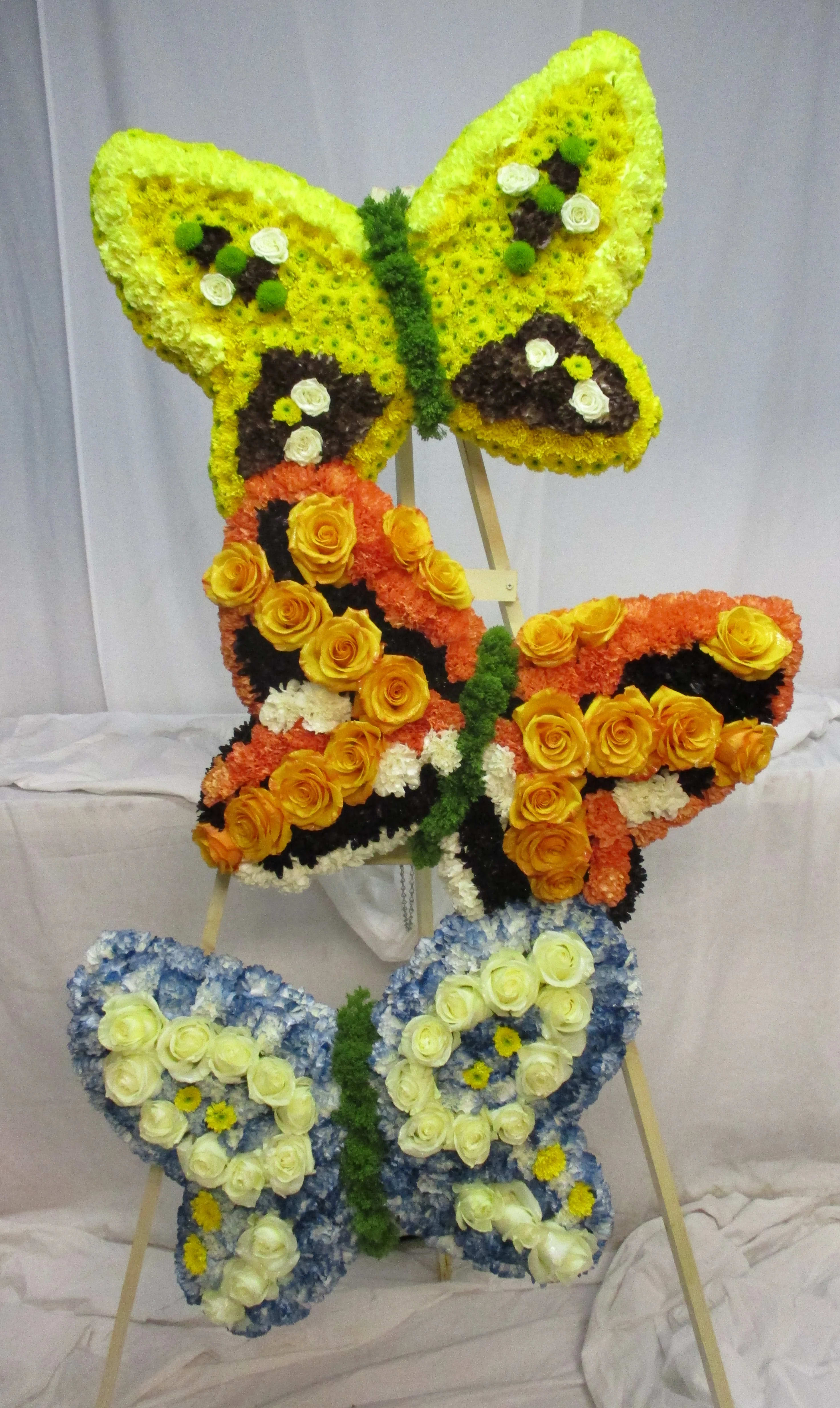 Butterfly-shaped floral display on an easel in yellow, orange, blue, and white.