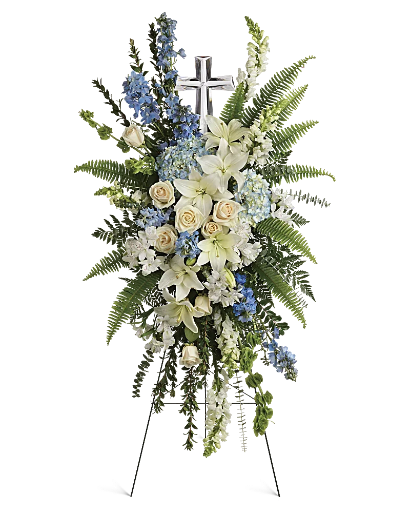 Standing funeral spray with white lilies, cream roses, and blue flowers around a cross