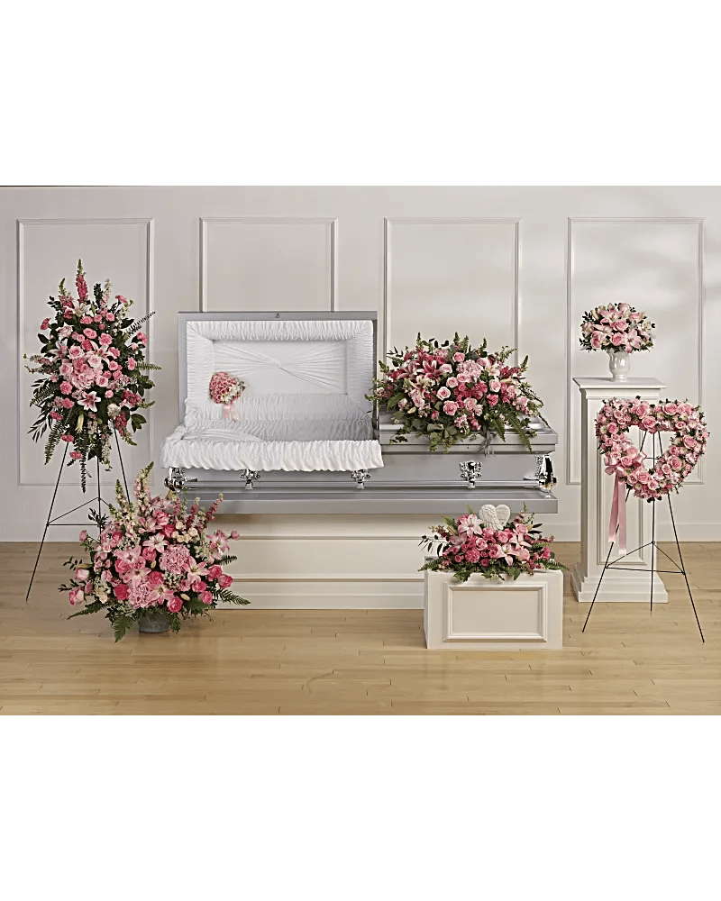 Pink floral funeral casket spray with matching arrangements around a white casket