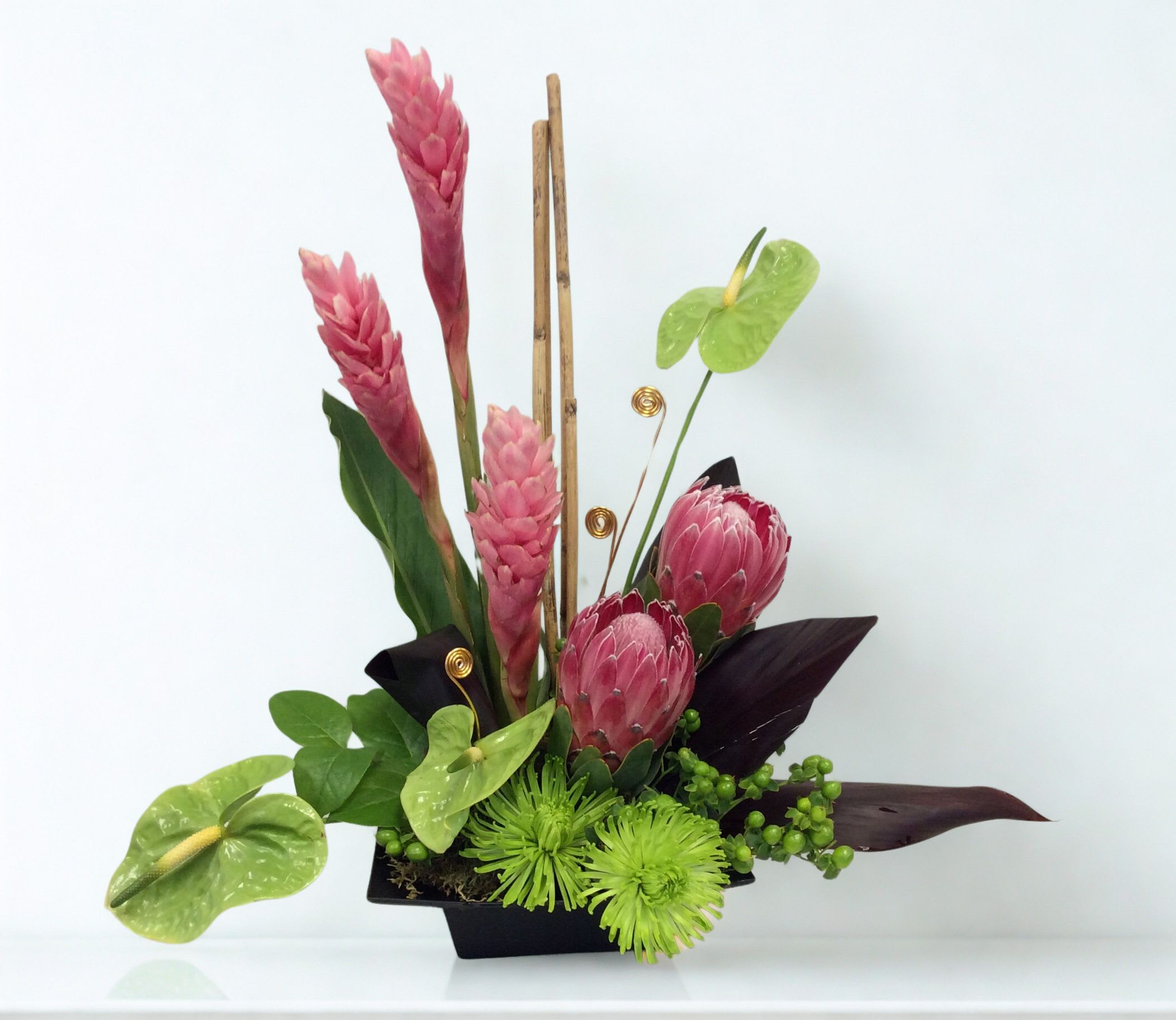 Pink tropical flowers arranged in a black container with green accents