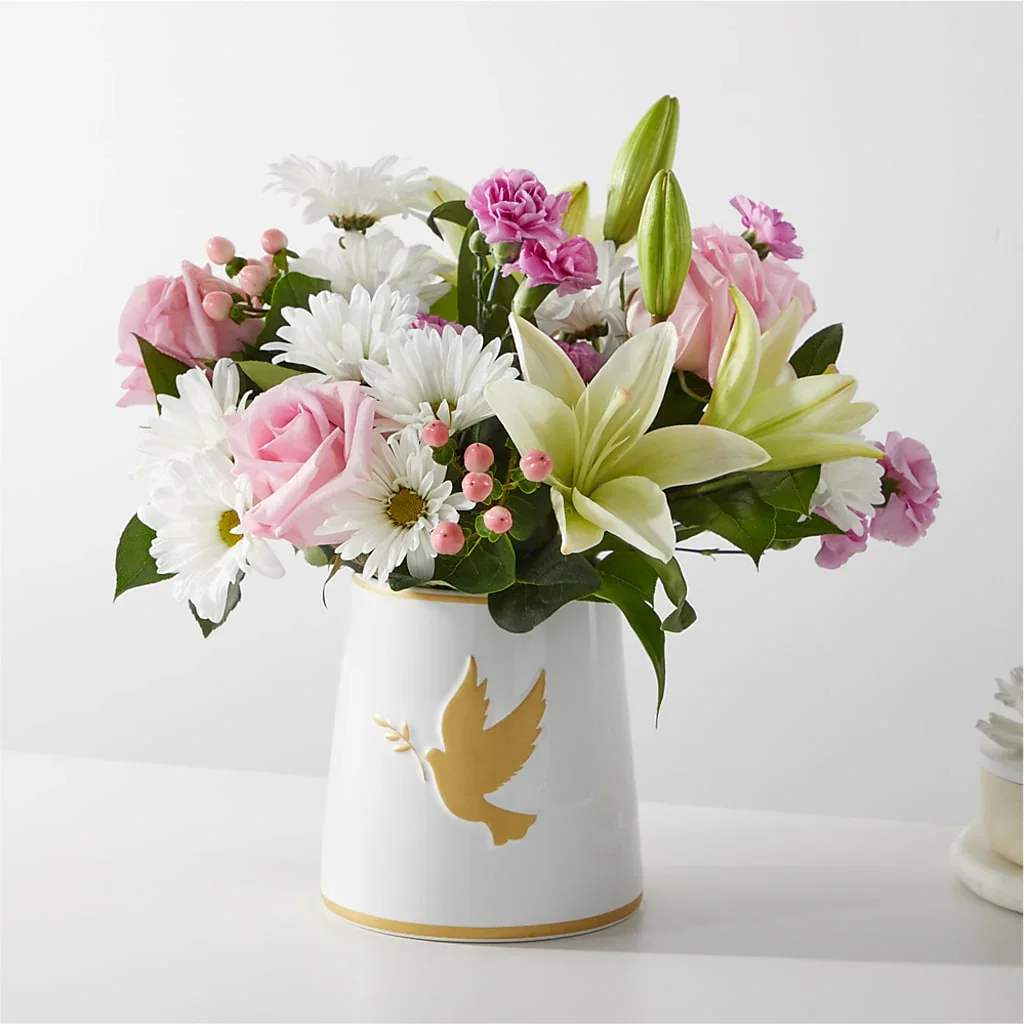 Pink and white mixed flower arrangement in a white vase with a gold dove