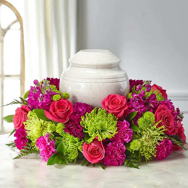 Pink roses and magenta flowers arranged around a white urn.