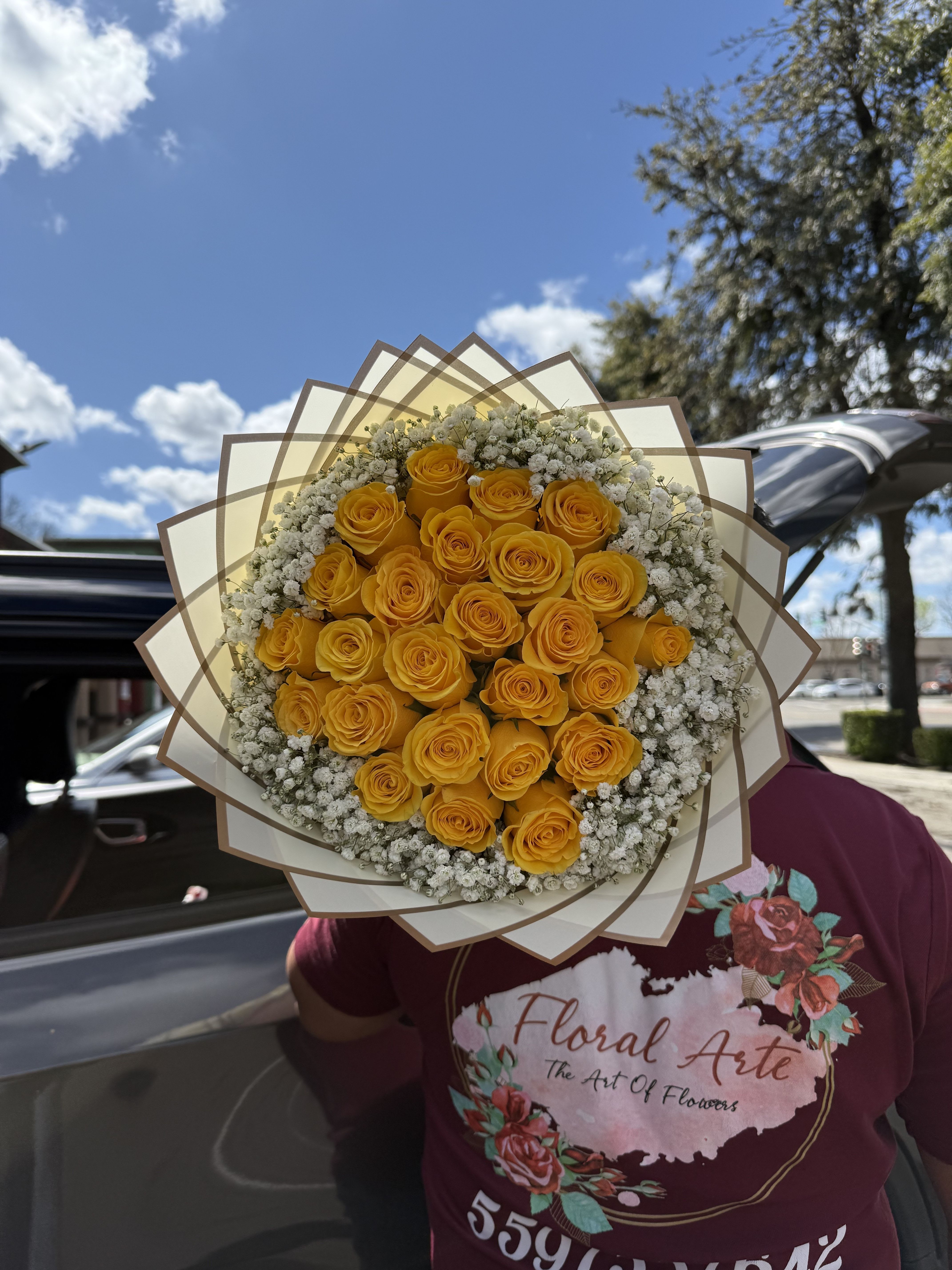 Bouquet of yellow roses with white filler flowers wrapped in layered paper