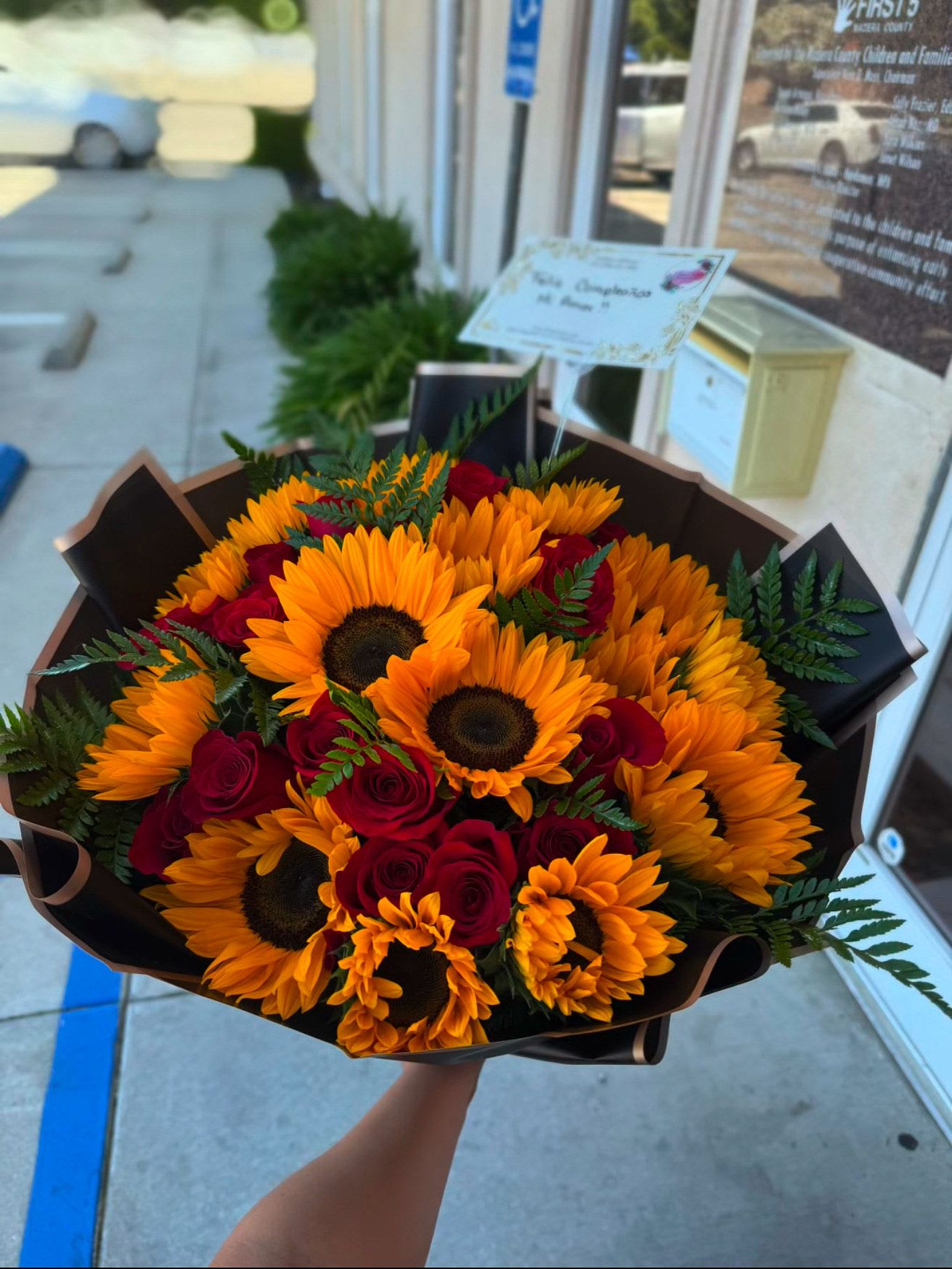 Bouquet of sunflowers and red roses wrapped in dark paper