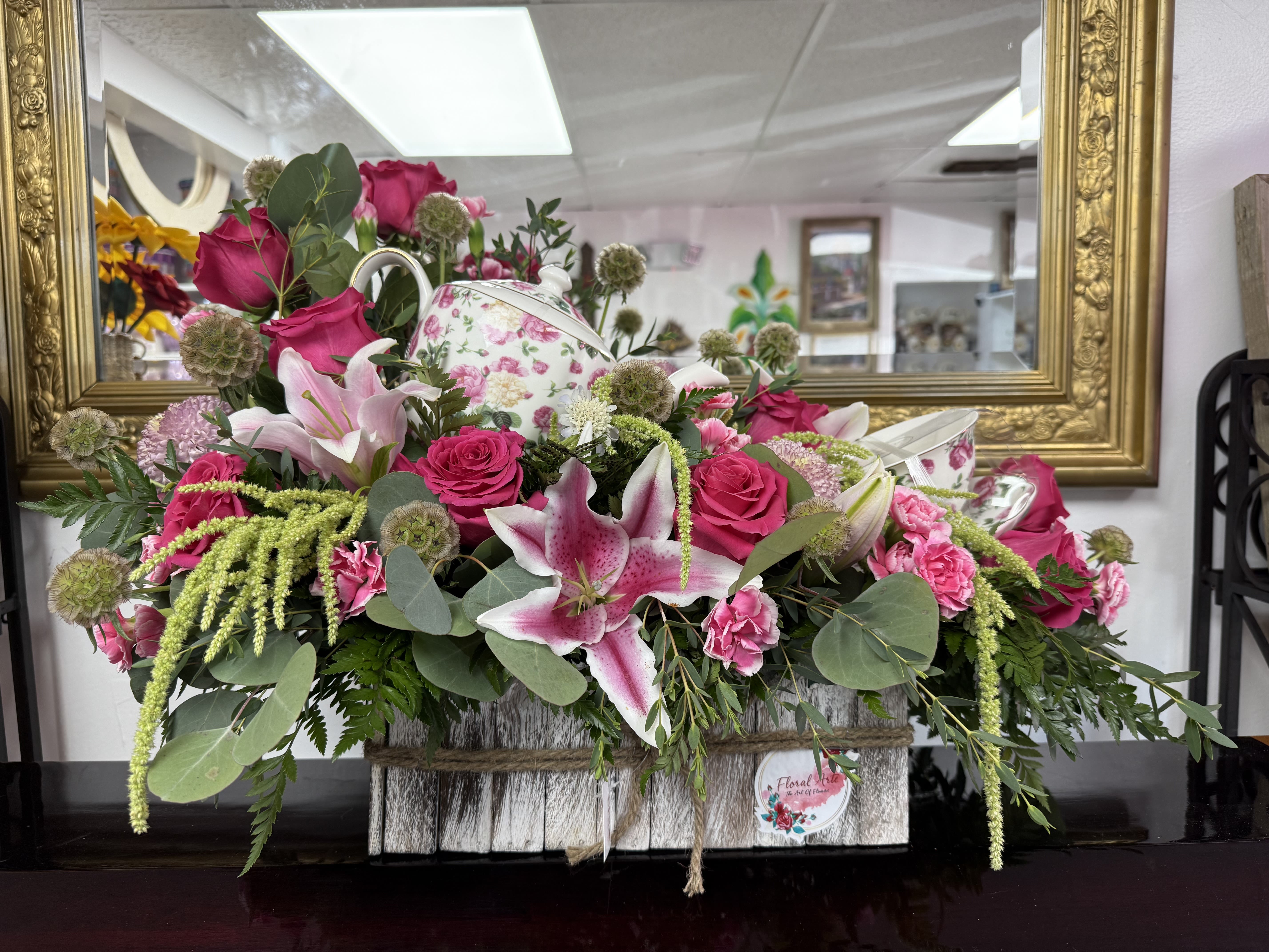 Pink roses and lilies arranged in a floral basket with a teapot centerpiece