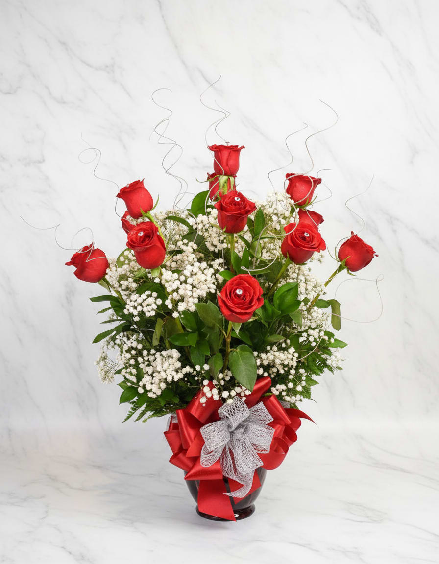 Red roses arranged in a glass vase with white baby's breath and ribbon