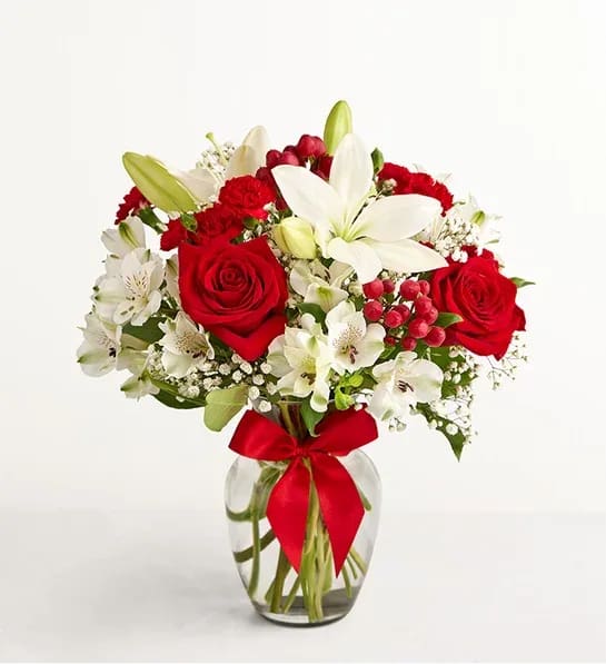 Red roses and white lilies in a glass vase with a red ribbon