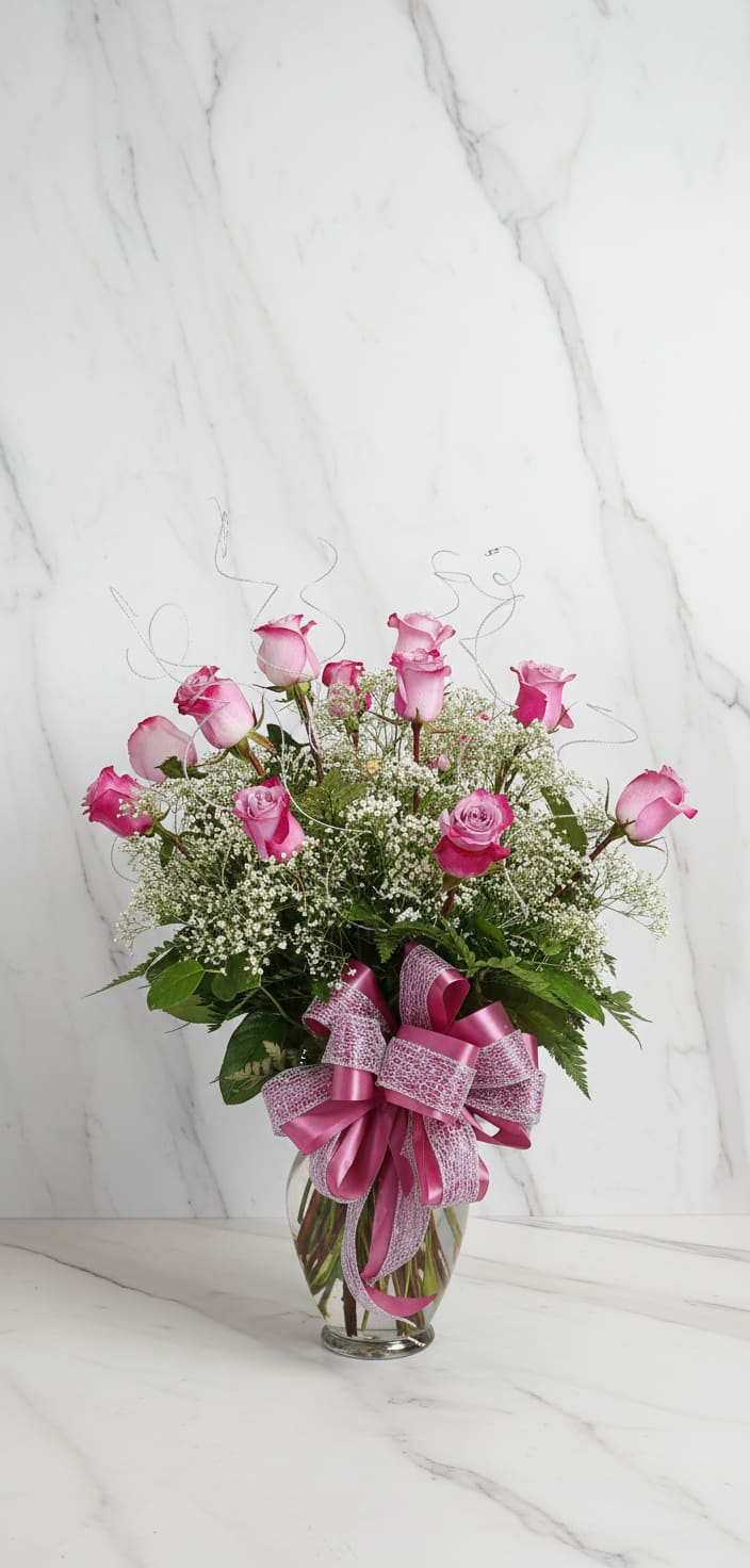 Pink roses in a clear glass vase with a large ribbon bow