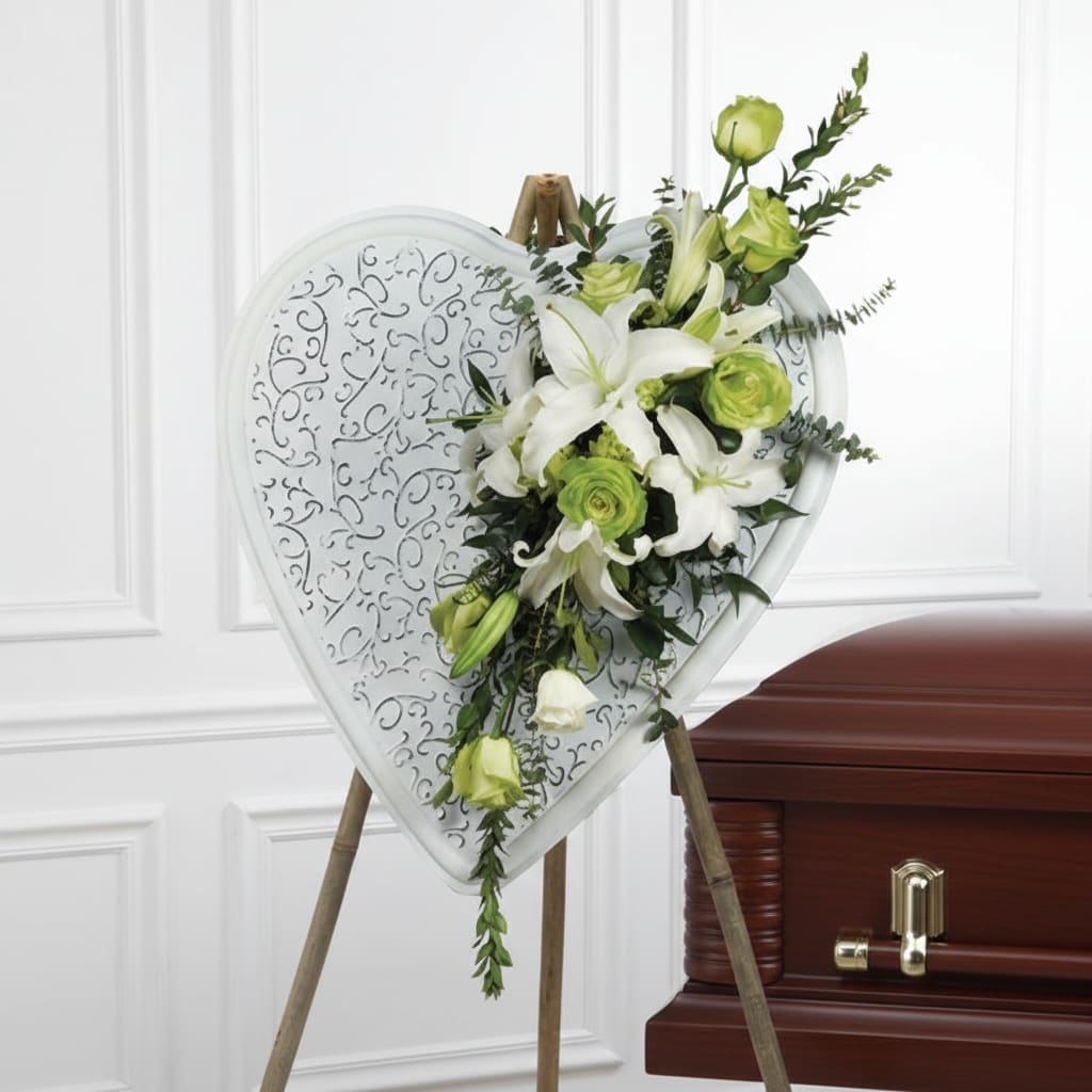 Heart-shaped floral spray on an easel beside a casket