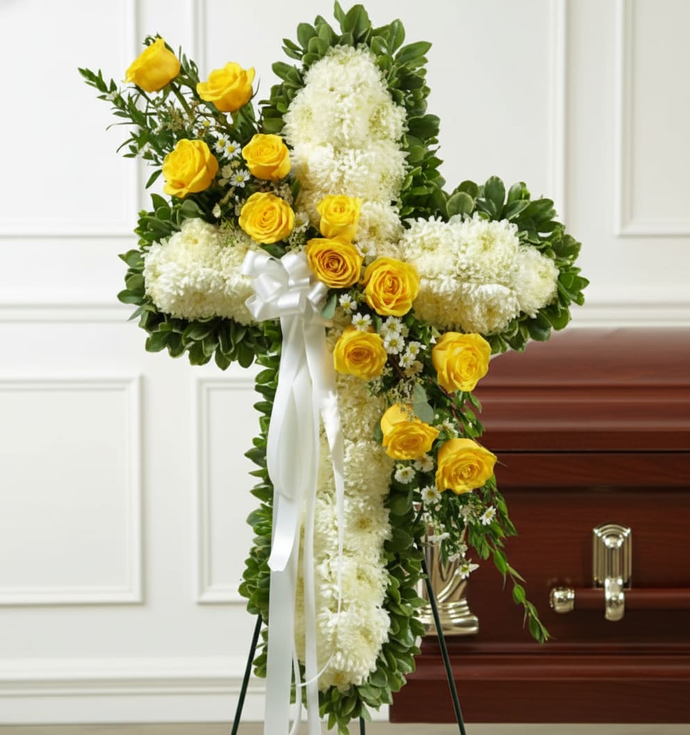 White floral cross with yellow roses and ribbon on a stand