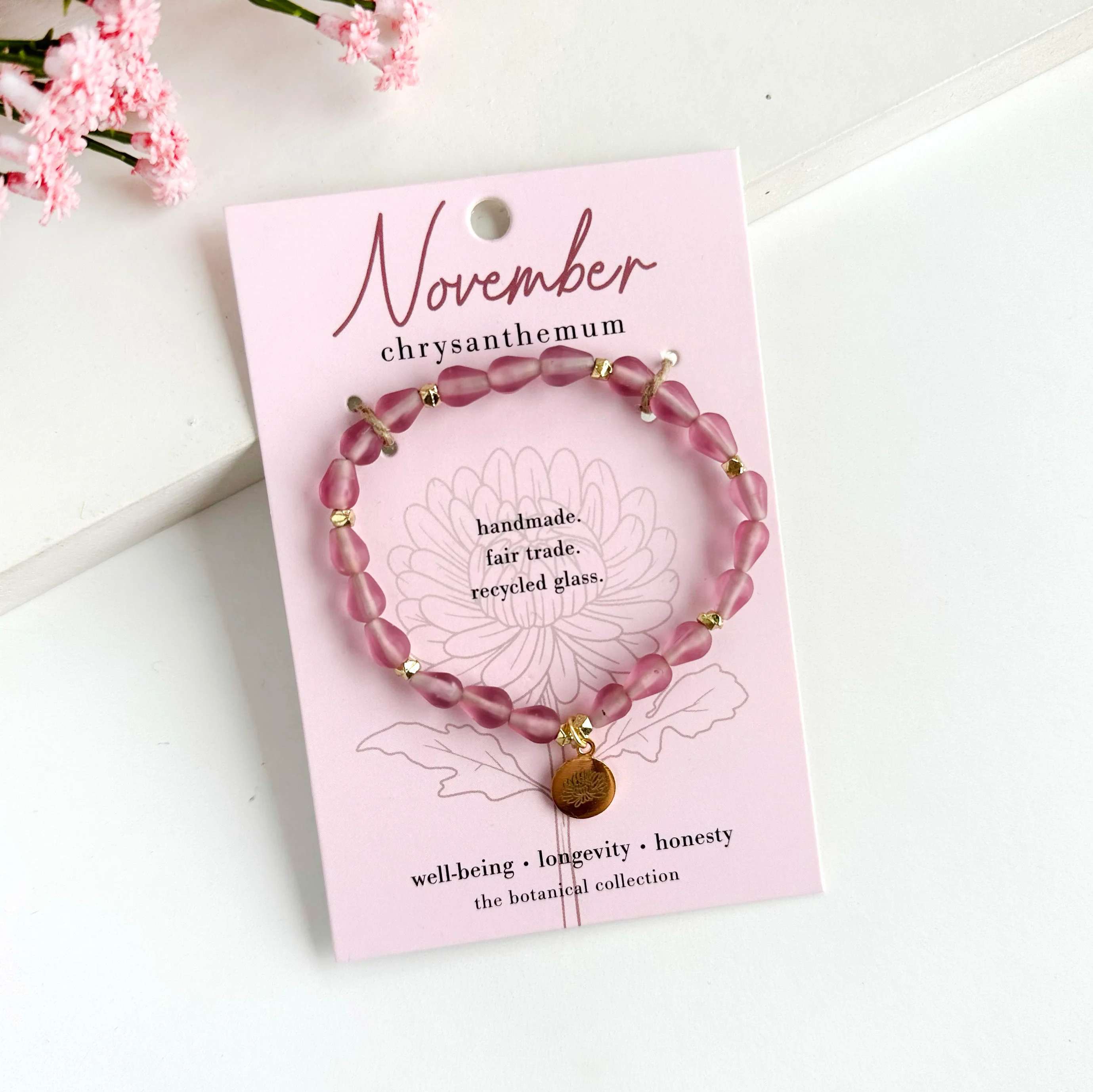 November-Birth Flower Bracelet - Hello, November! ? Part of our Botanical Collection, the November Bracelet is crafted from soft pink glass beads, brass accent beads, and features a chrysanthemum charm. Great for gifting, the card features the chrysanthemum and it's symbols of well-being, longevity and honesty, along with a garden-inspired quote. This bracelet also benefits an urban community garden project!  The semi-opaque beads have a satin, frosted texture and are handmade from recycled glass. The flower charm is 24k gold plated.   Sustainably handmade by women artisans in India.