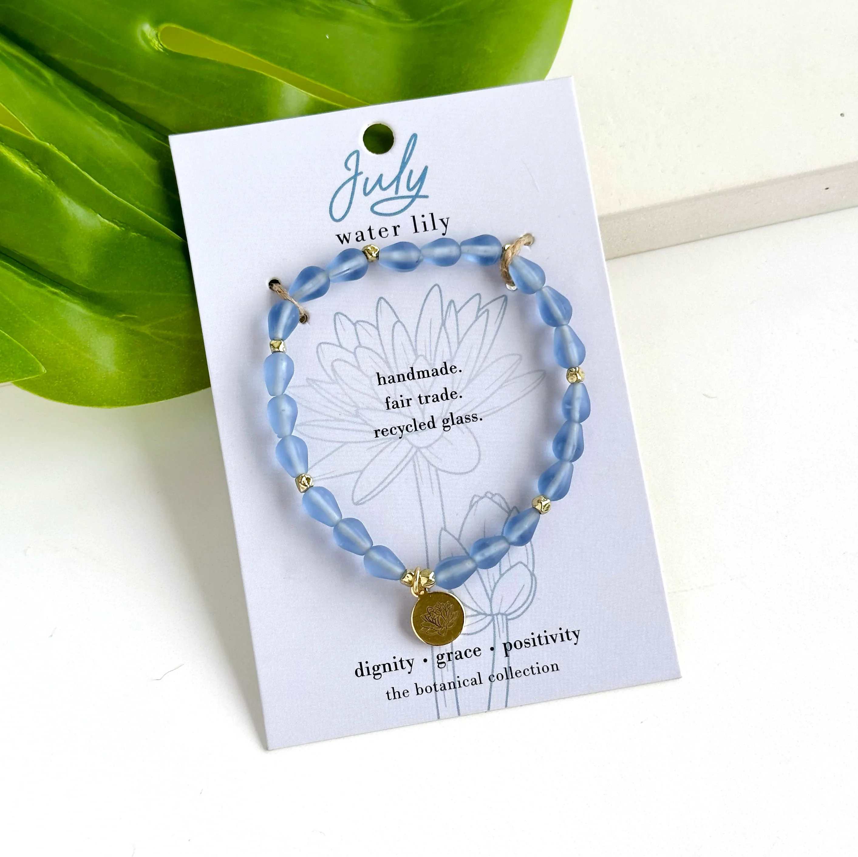 July-Birth Flower Bracelet - Hello, July! ? Part of our Botanical Collection, the July Bracelet is crafted from rich blue glass beads, brass accent beads, and features a water lily charm. Great for gifting, the card features the water lily and it's symbols of dignity, grace and positivity, along with a garden-inspired quote. This bracelet also benefits an urban community garden project!  The semi-opaque beads have a satin, frosted texture and are handmade from recycled glass. The flower charm is 24k gold plated.   Sustainably handmade by women artisans in India.