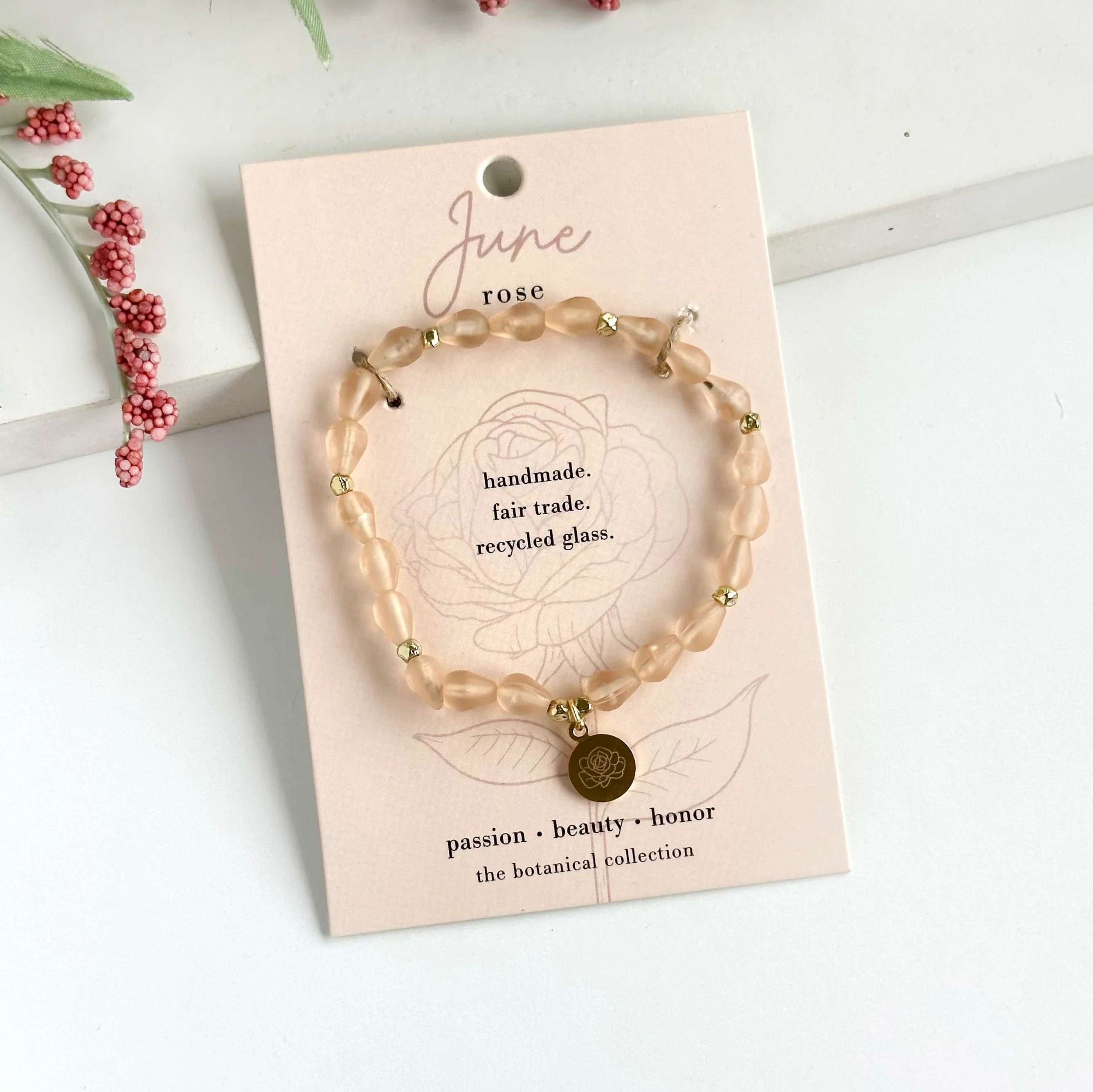 June-Birth Flower Bracelet - Hello, June!  Part of our Botanical Collection, the June Bracelet is crafted from soft pink glass beads, brass accent beads, and features a rose charm. Great for gifting, the card features the rose and it's symbols of passion, beauty &amp; honor, along with a garden-inspired quote. This bracelet also benefits an urban community garden project!  The semi-opaque beads have a satin, frosted texture and are handmade from recycled glass. The flower charm is 24k gold plated.   Sustainably handmade by women artisans in India.