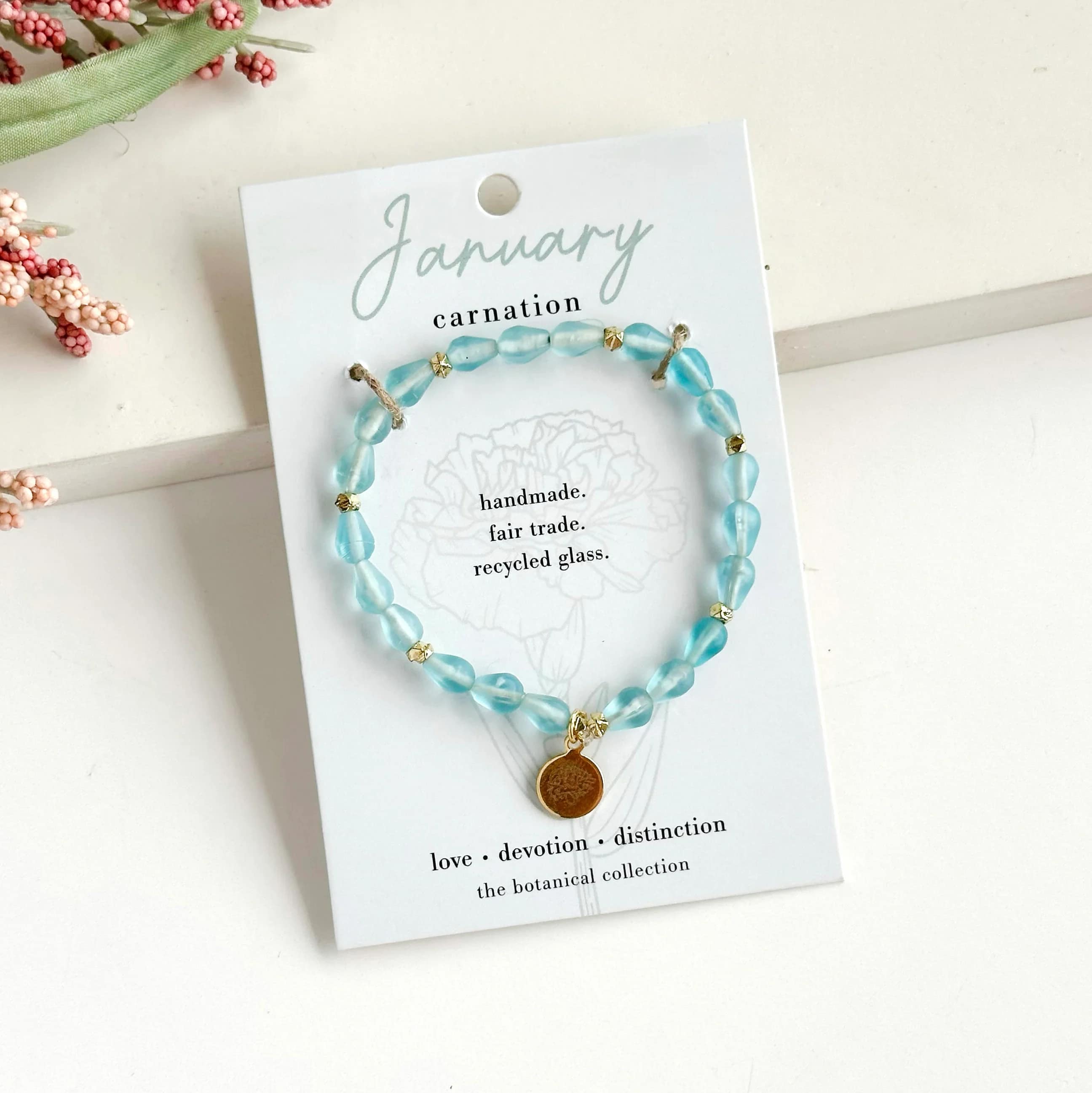January-Birth Flower Bracelet - Hello, January! ? Part of our Botanical Collection, the January Bracelet is crafted from light blue glass beads, brass accent beads, and features a carnation charm. Great for gifting, the card features the carnation and it's symbols of love, devotion and distinction, along with a garden-inspired quote. This bracelet also benefits an urban community garden project!  The semi-opaque beads have a satin, frosted texture and are handmade from recycled glass. The flower charm is 24k gold plated.   Sustainably handmade by women artisans in India.