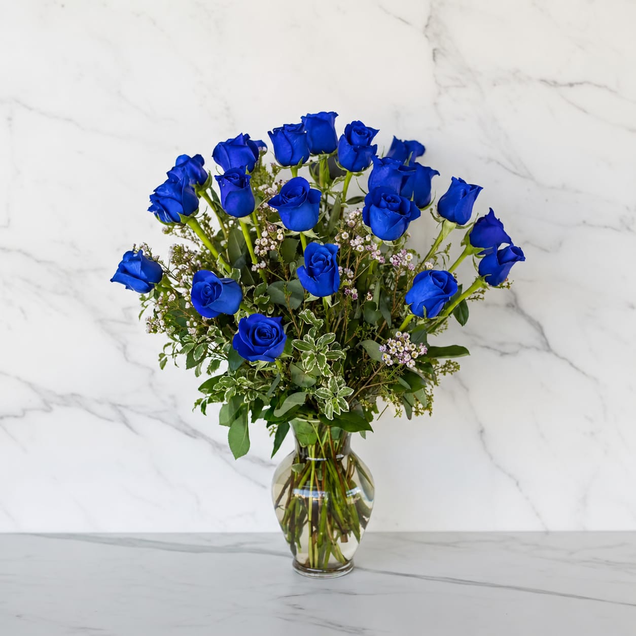 2 Dozen Long Stem Blue Roses - 24 Blue Roses Vase Arrangement    A stunning arrangement of 24 premium blue roses, artfully designed with fresh greenery in a clear glass vase. Elegant, unique, and unforgettable—perfect for celebrating life’s special moments.