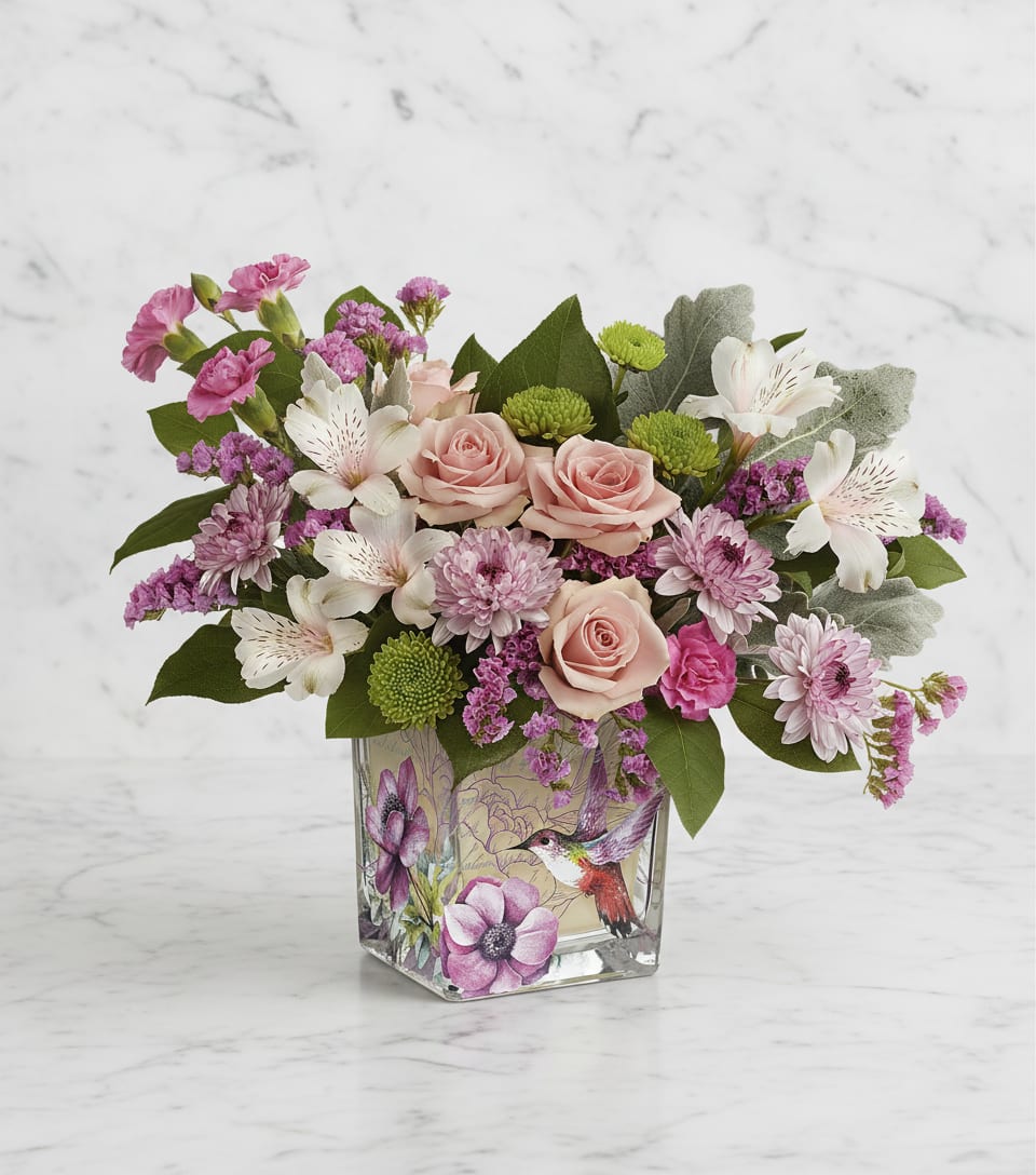 Pink roses and mixed blooms arranged in a square glass vase