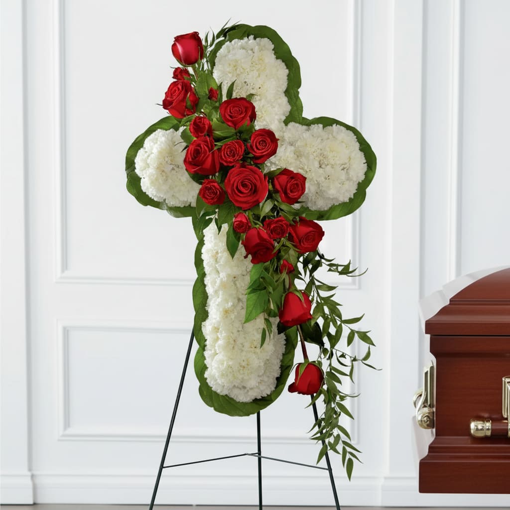 Cross-shaped floral tribute with red roses and white blooms on a stand