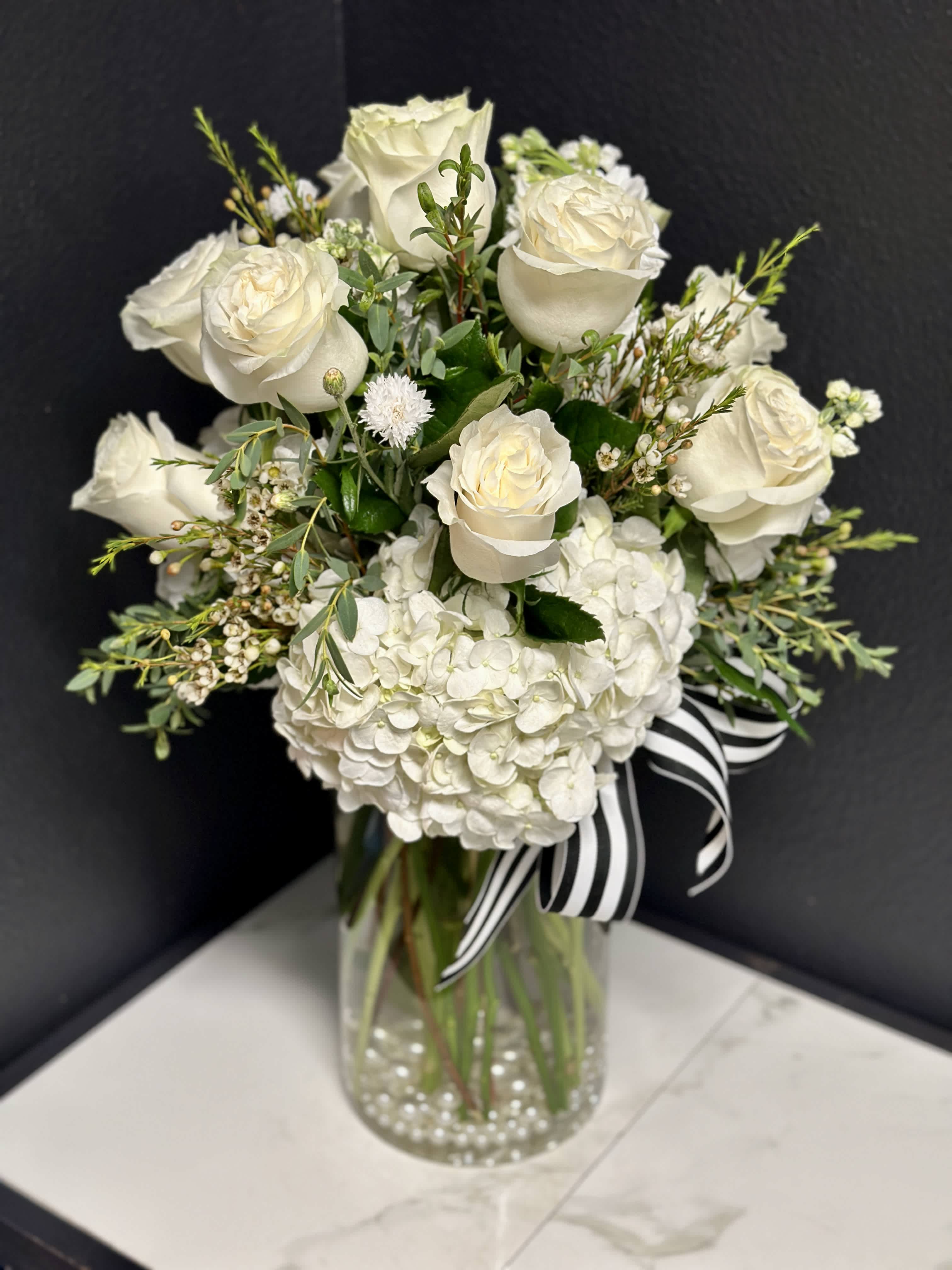 White roses and hydrangeas in a glass vase with a striped ribbon