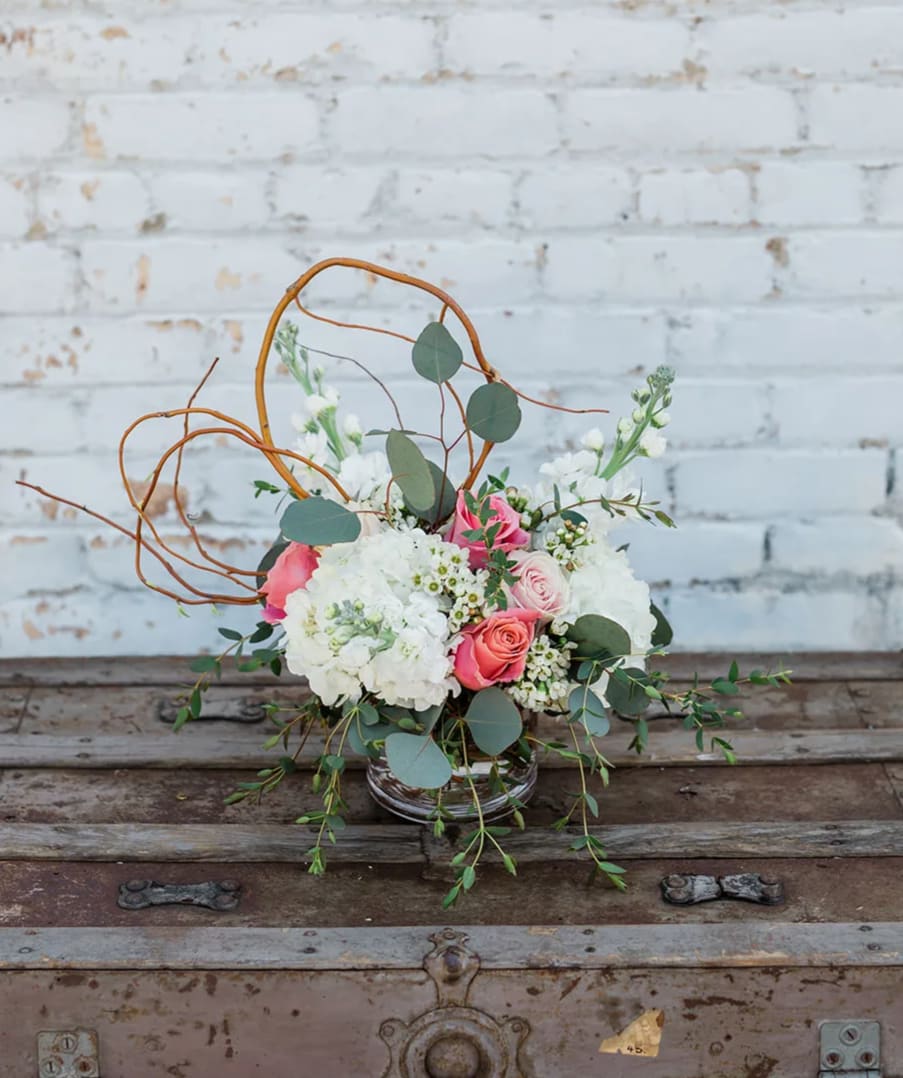 Pink and white floral arrangement in a glass vase with curly branches