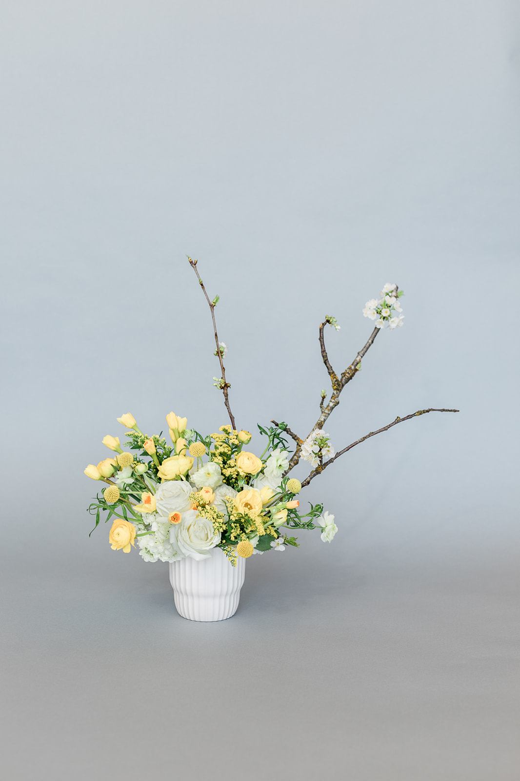 Yellow and white floral arrangement in a white vase with branching stems