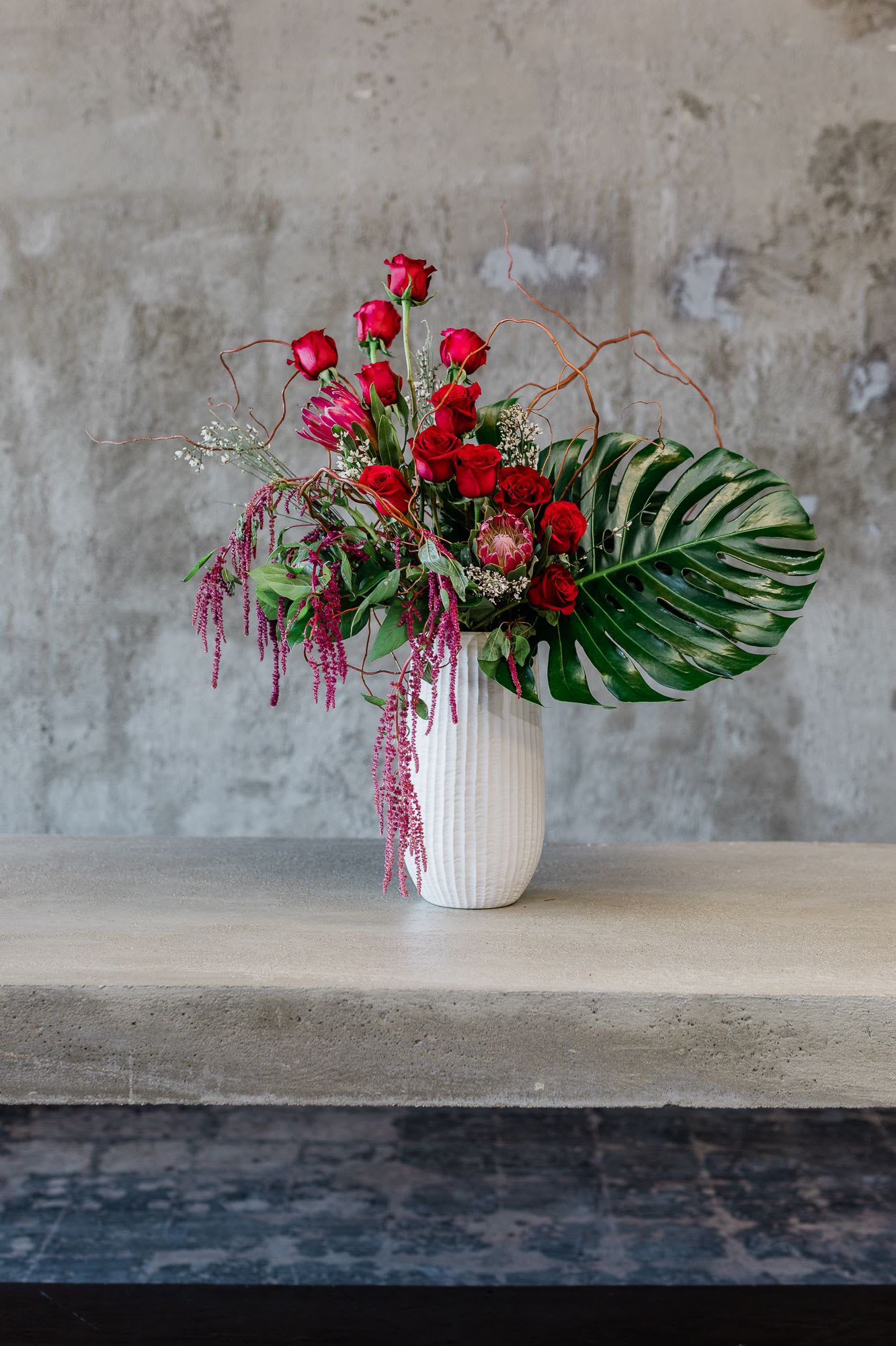 Red rose arrangement in a white vase with tropical leaves