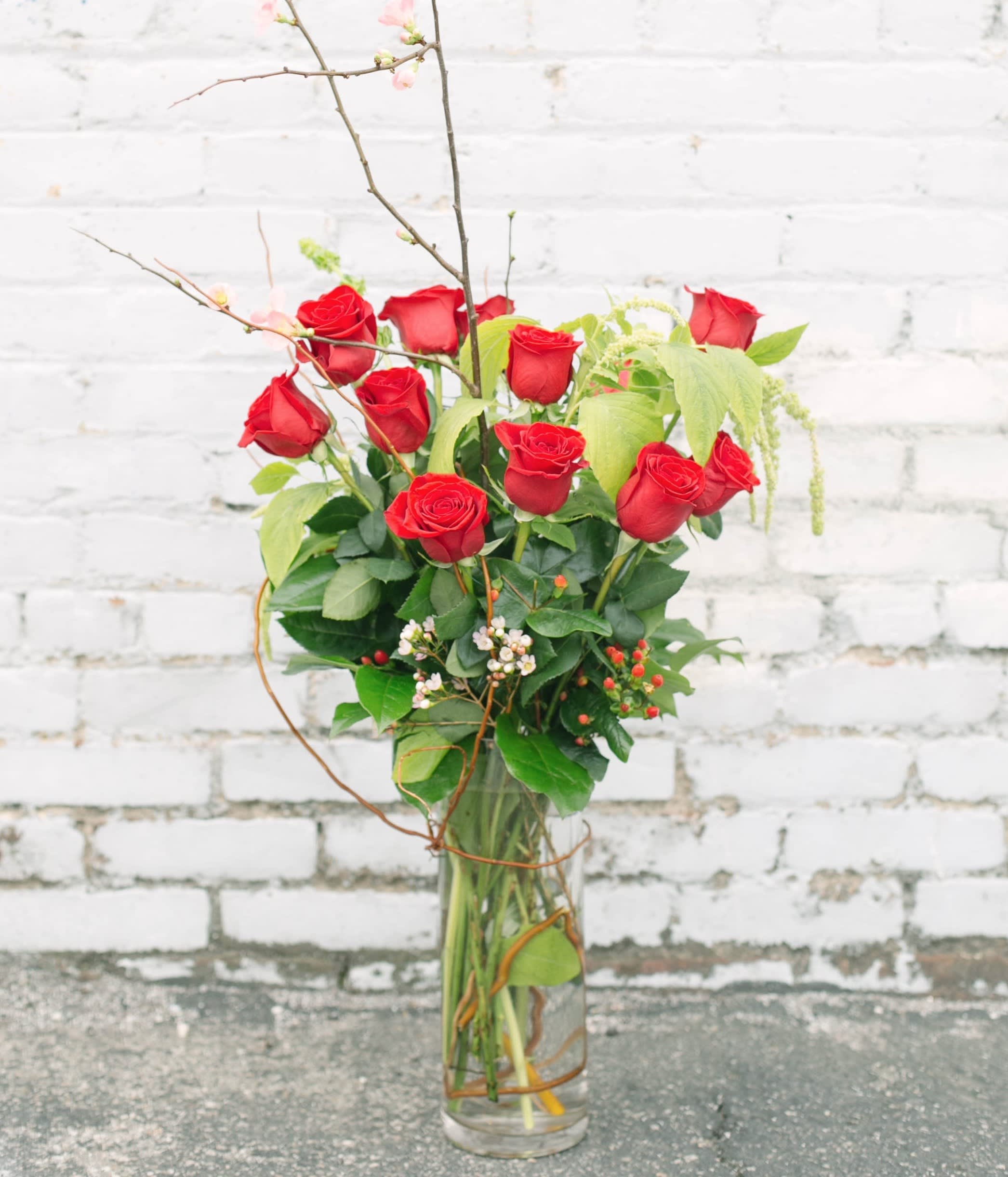 Red roses arranged in a tall glass vase with branches and greenery