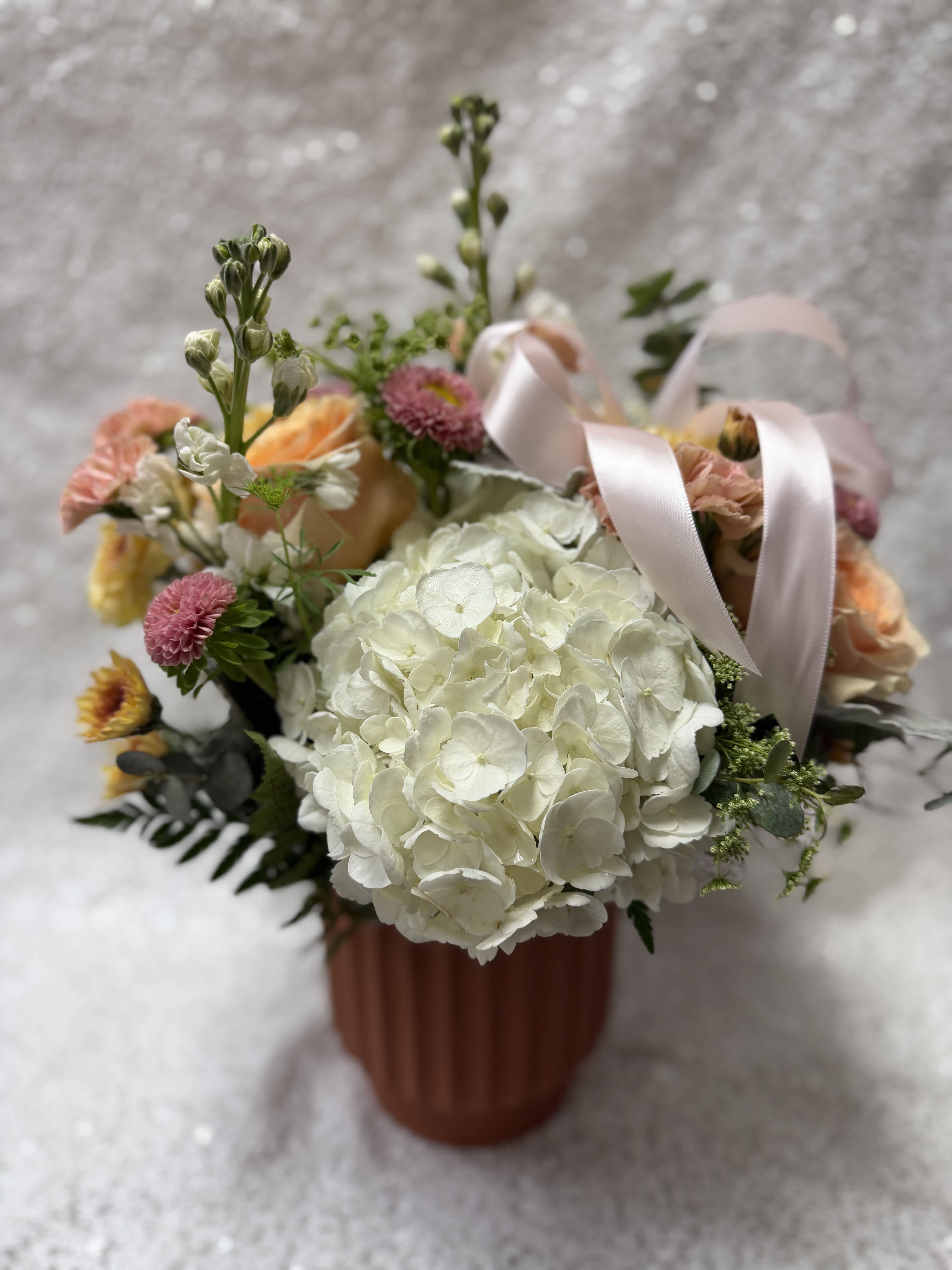 Bouquet of white hydrangea, peach roses, and pink flowers in a ribbed vase