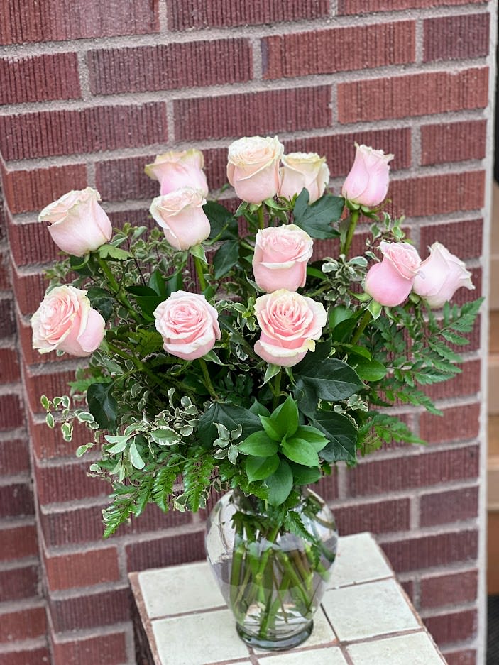 Pink roses arranged in a clear glass vase with mixed greenery