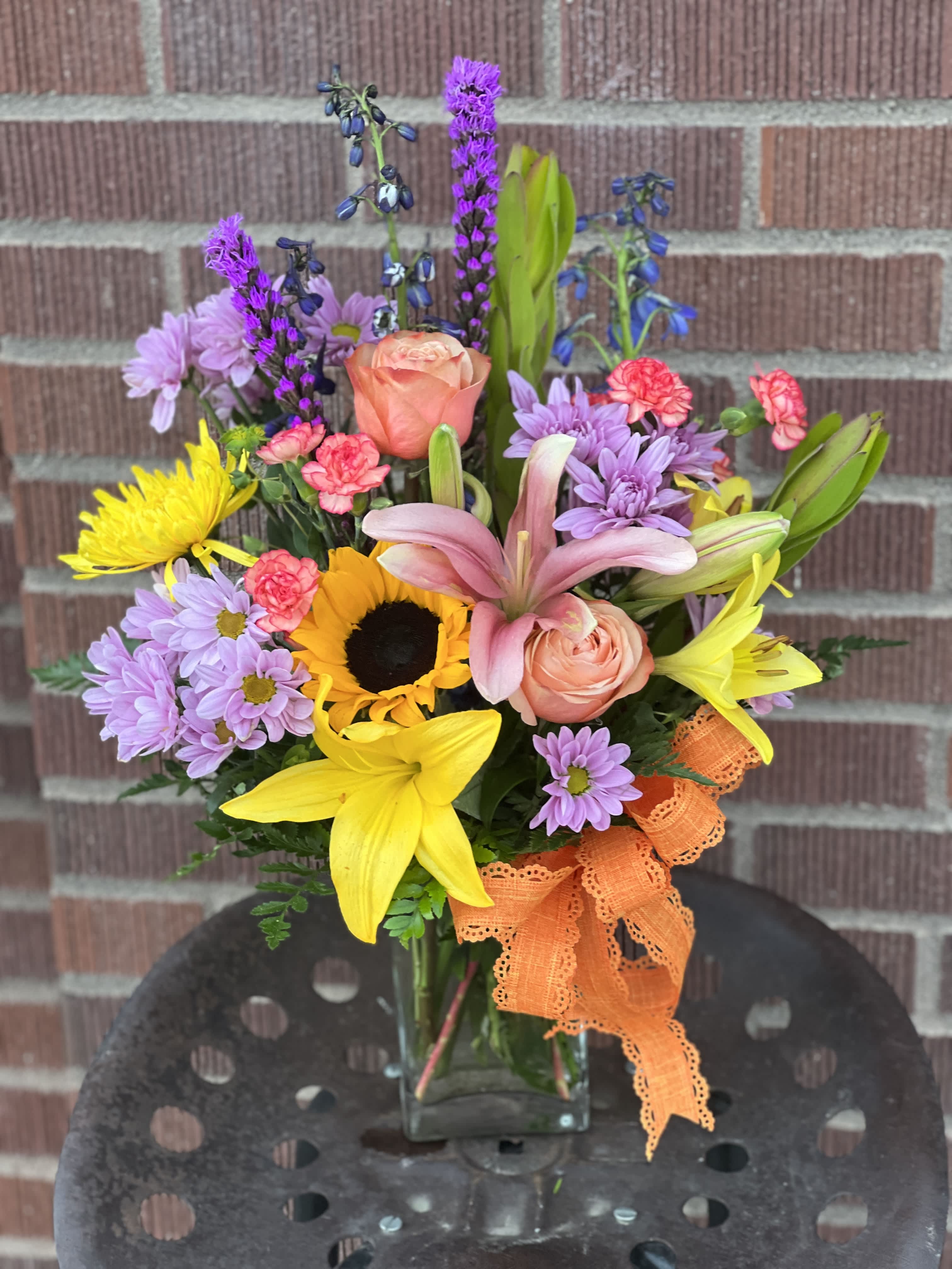 Mixed bouquet with sunflowers, lilies, roses, and purple daisies in a glass vase