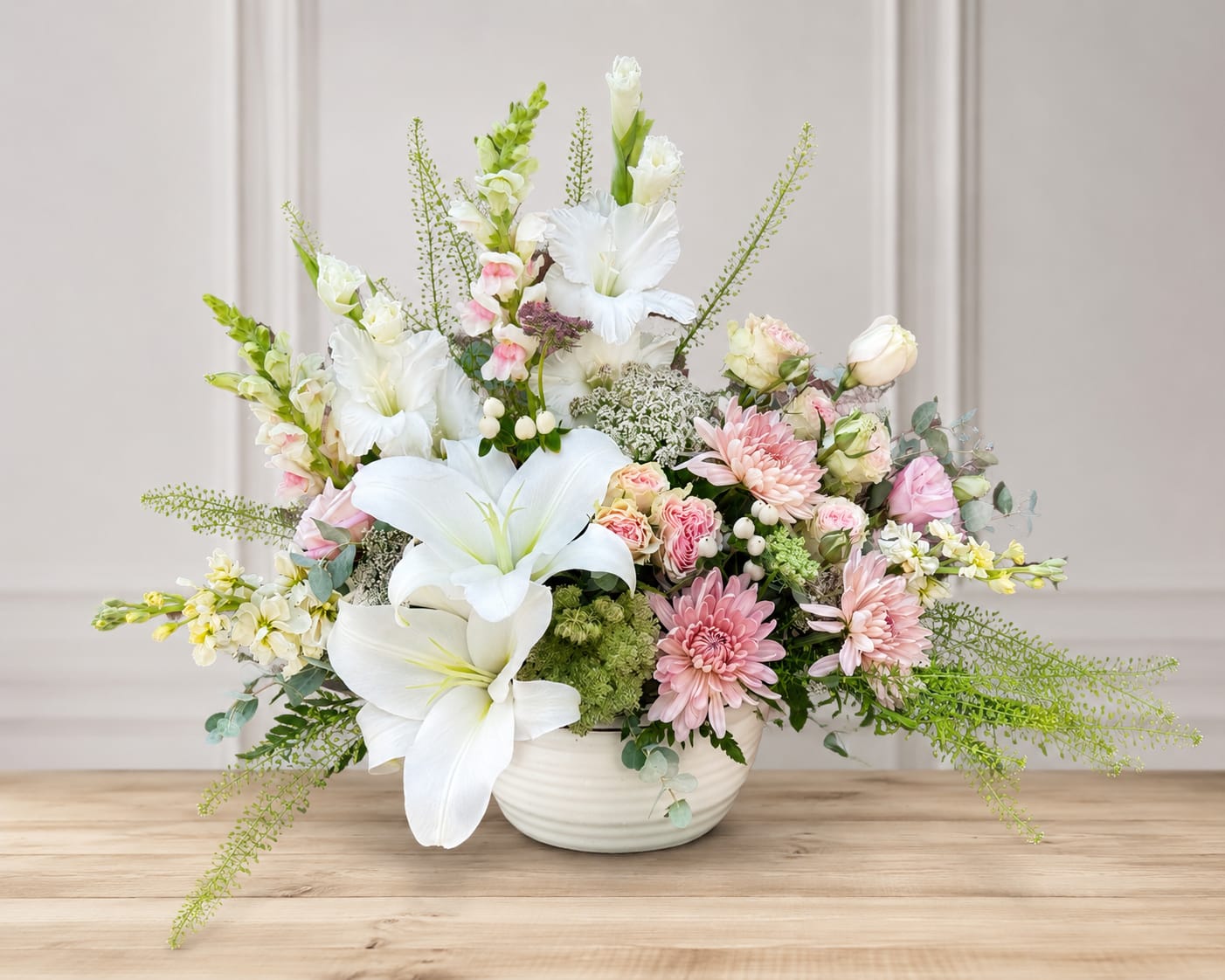 White lilies and pink mixed flowers arranged in a white bowl vase