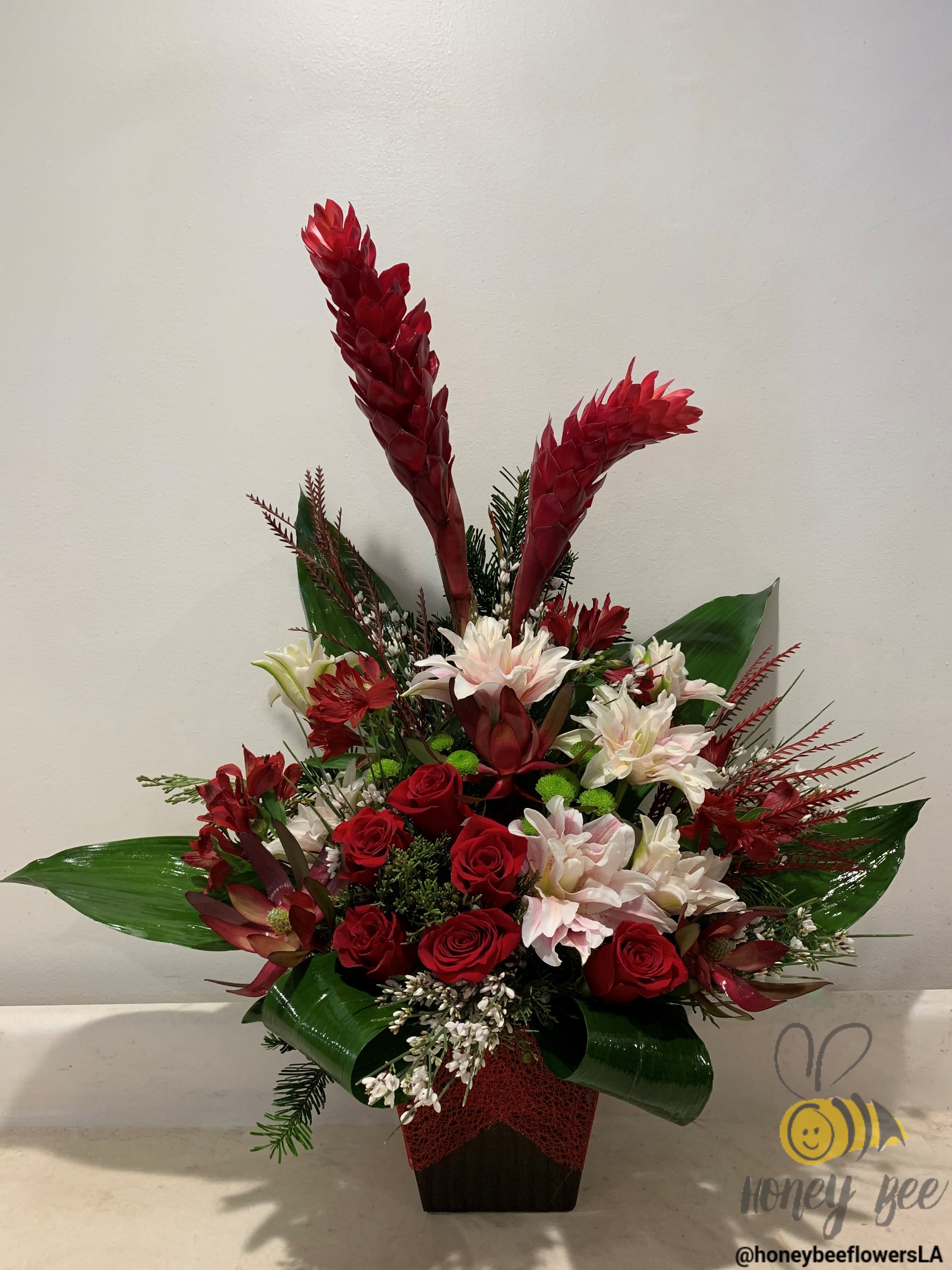 Tropical floral arrangement with red roses and white blooms in a dark vase