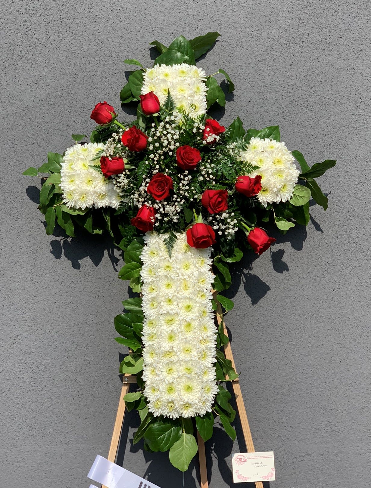 Cross-shaped floral tribute with white chrysanthemums and red roses on an easel