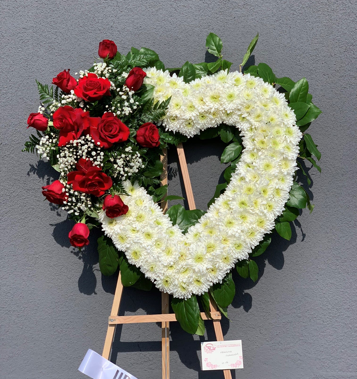 Heart-shaped floral wreath with red roses and white chrysanthemums on an easel