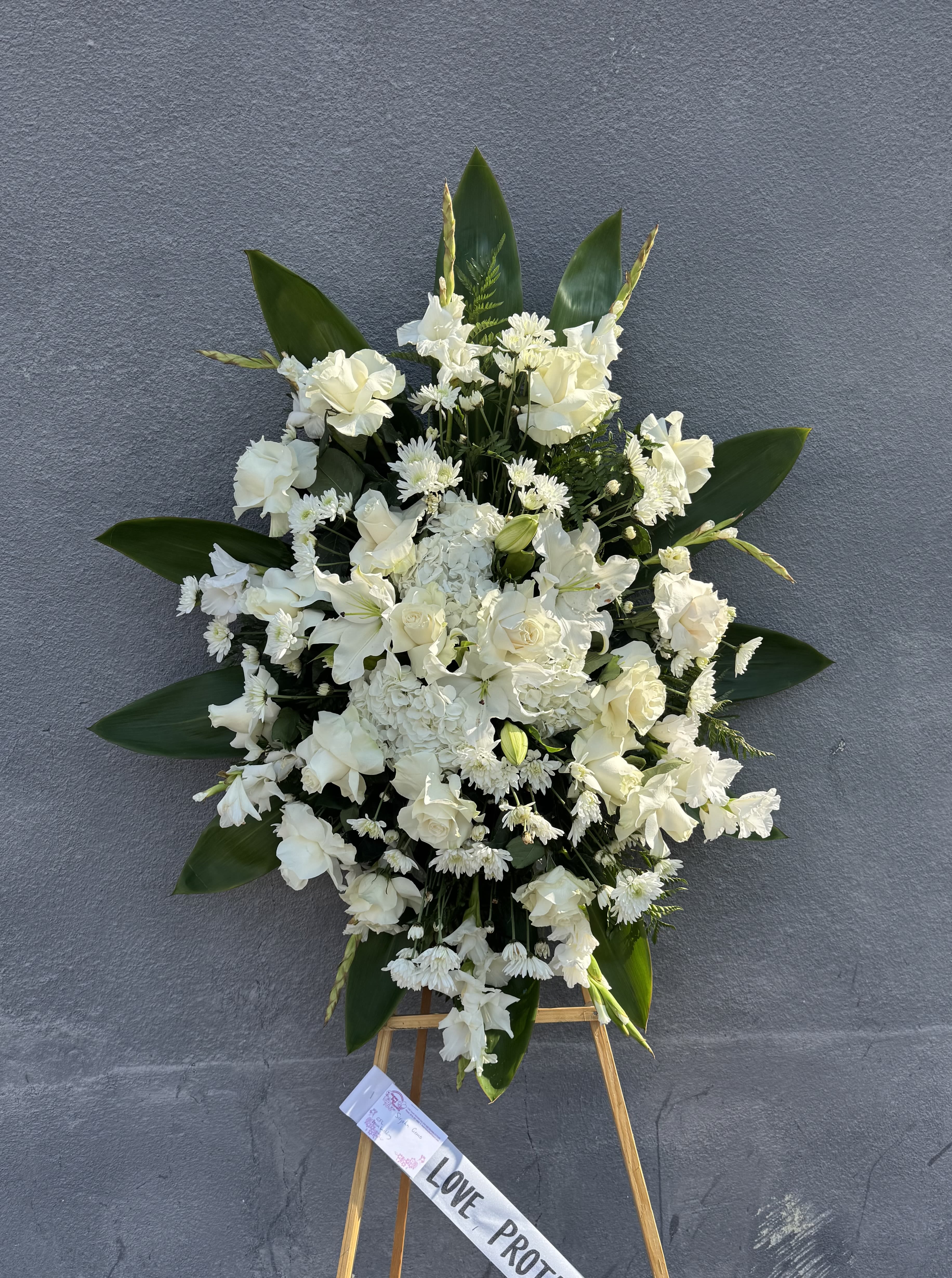 White funeral spray on an easel with a ribbon
