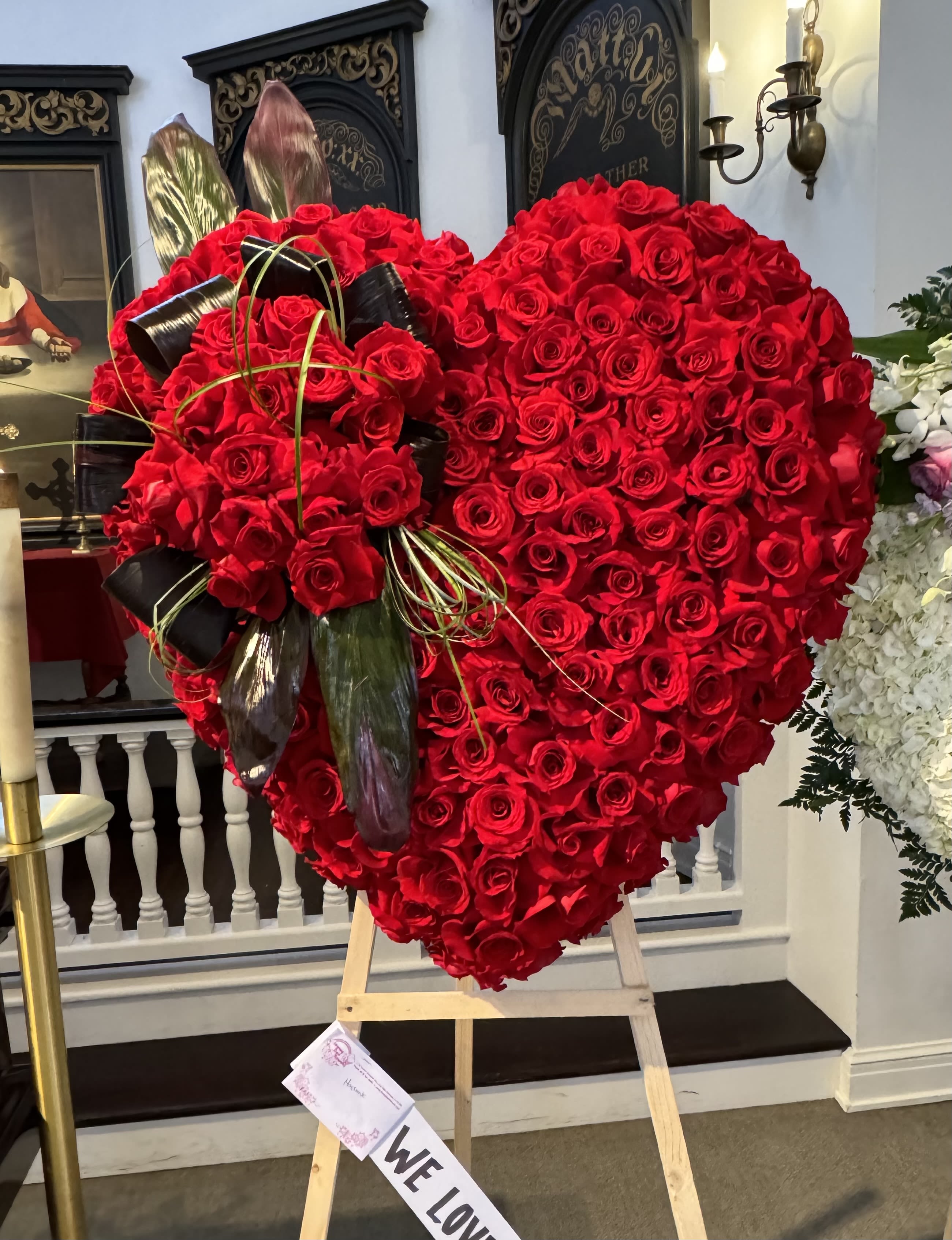 Heart-shaped red rose arrangement on an easel with black ribbon accents