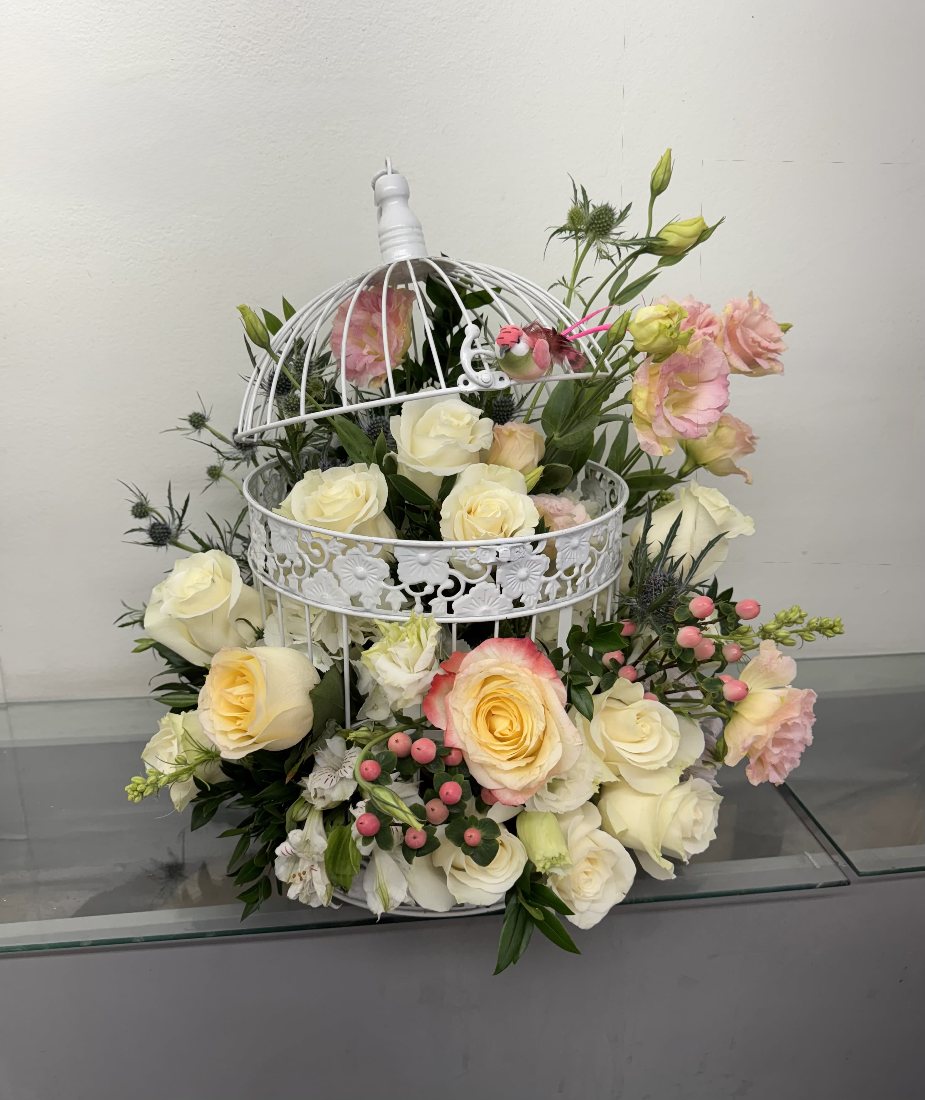White roses and pink lisianthus arranged in a decorative white birdcage.