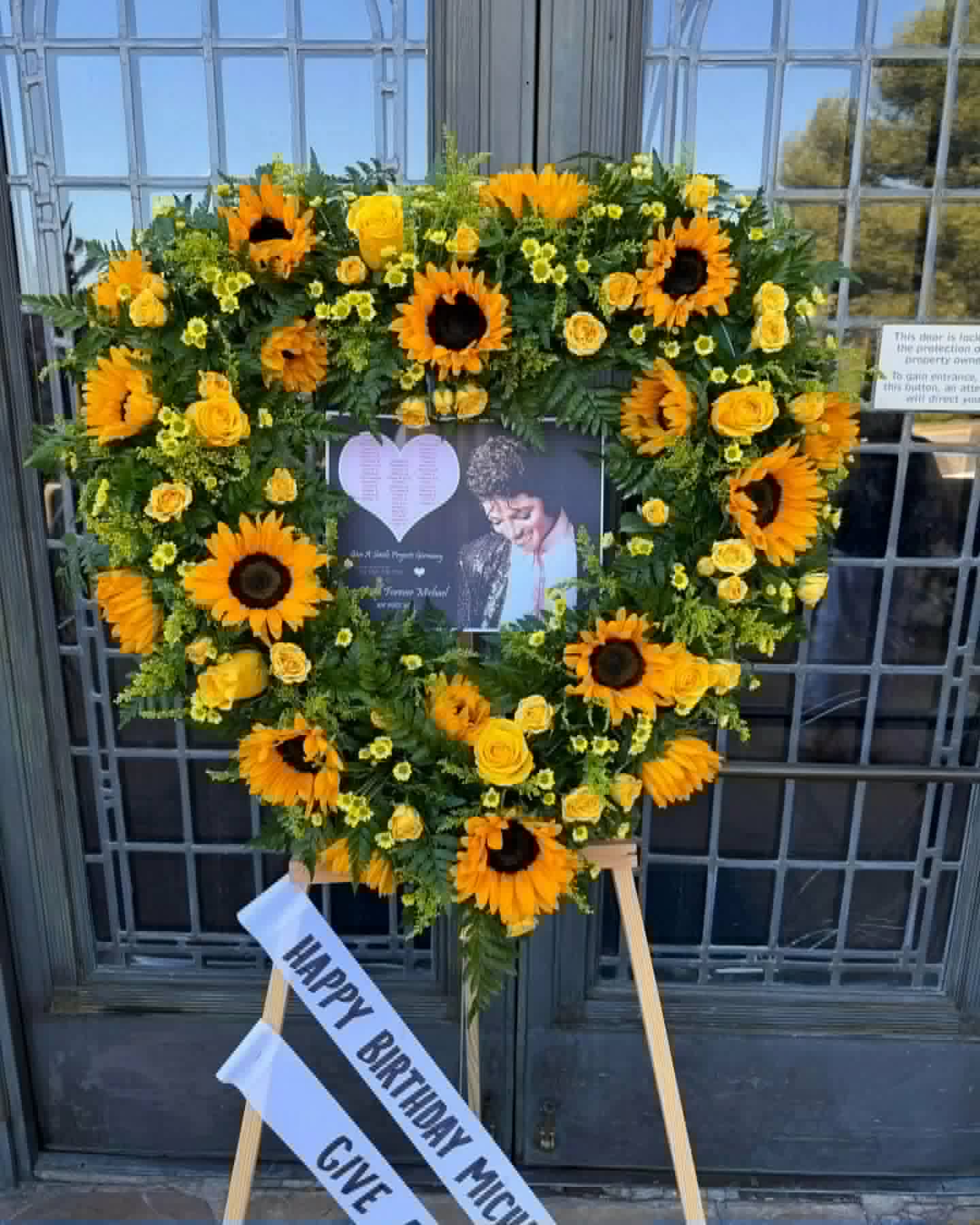 Heart-shaped sunflower and yellow rose standing wreath on an easel with a birthday ribbon