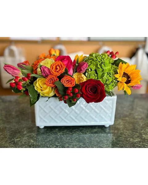 Mixed bouquet in a white rectangular vase with roses, tulips, and a sunflower