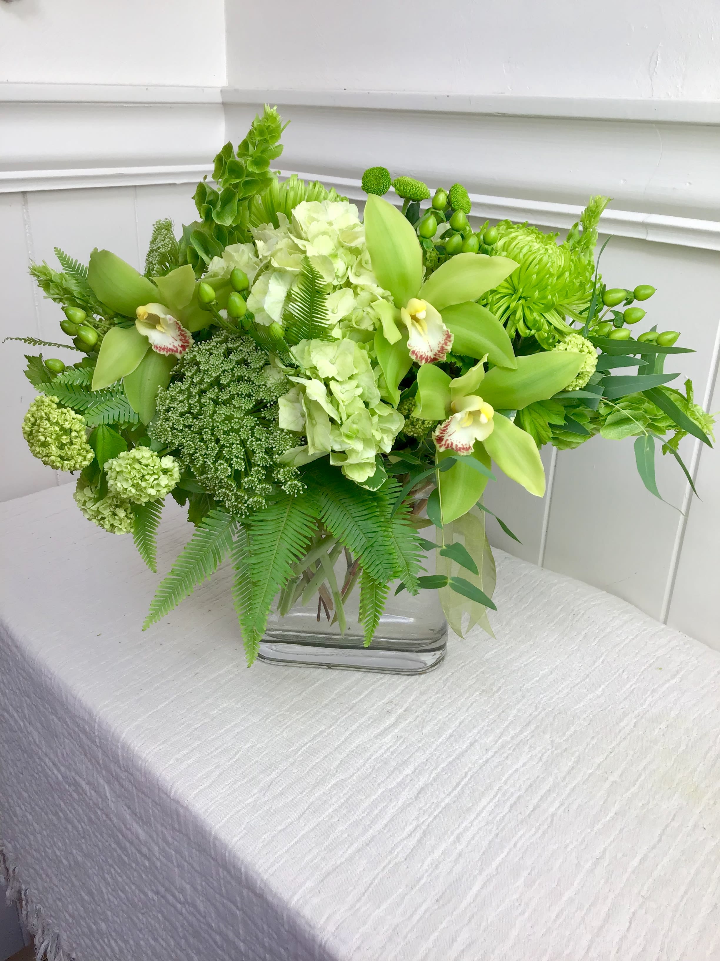Green floral arrangement in a glass vase with orchids and hydrangeas